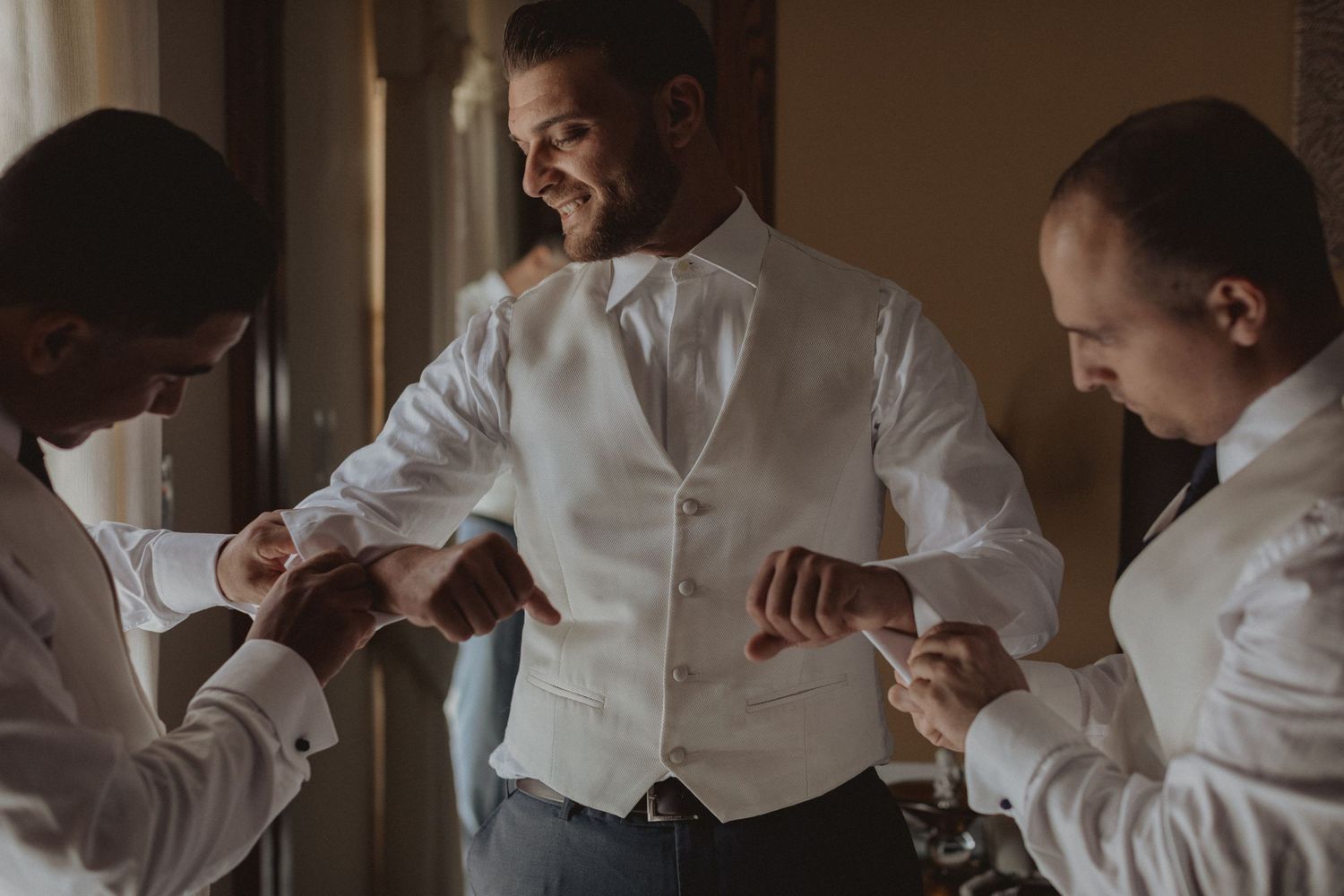 Groomsmen helping adjust formal attire before wedding ceremony.