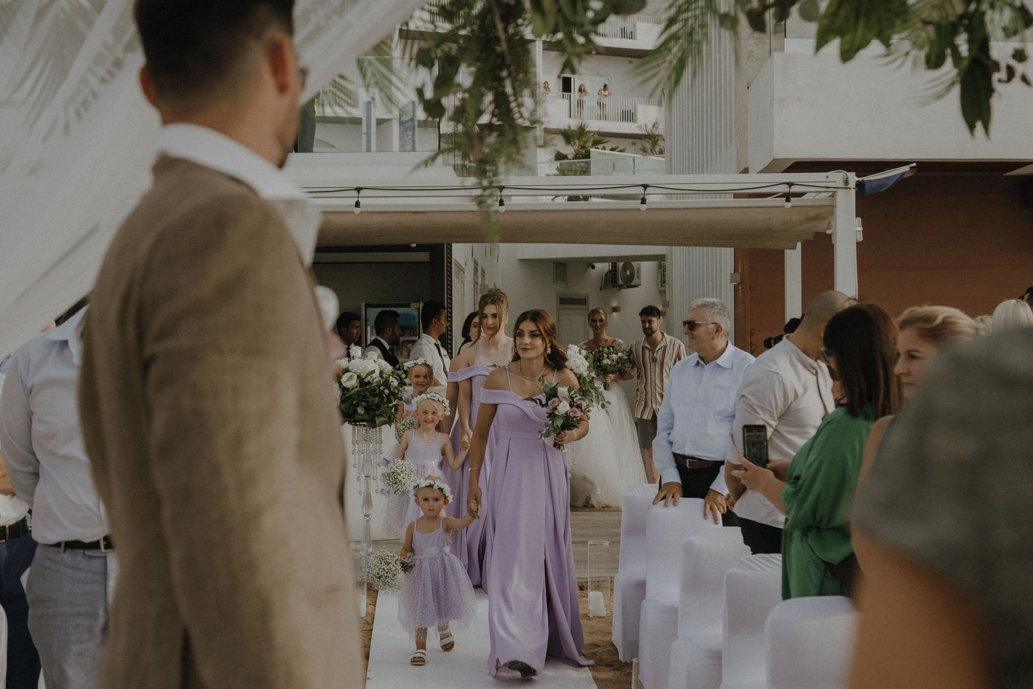 Beach wedding ceremony setup with white drapes and greenery overlooking ocean.