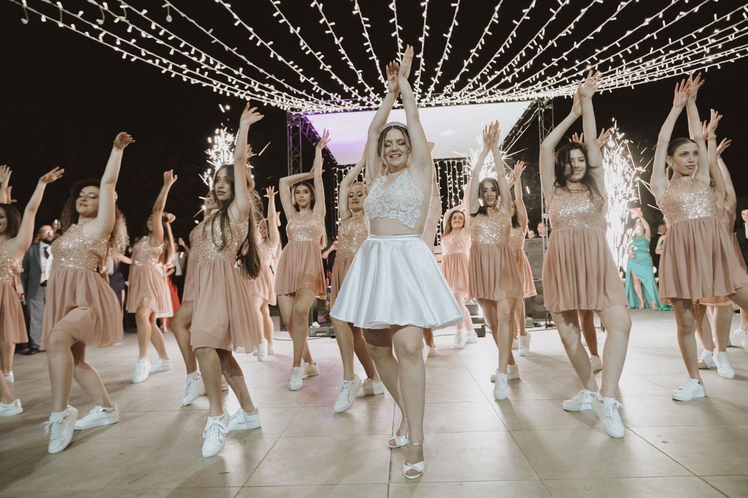 Group dance performance with raised arms under glittering string light decorations.