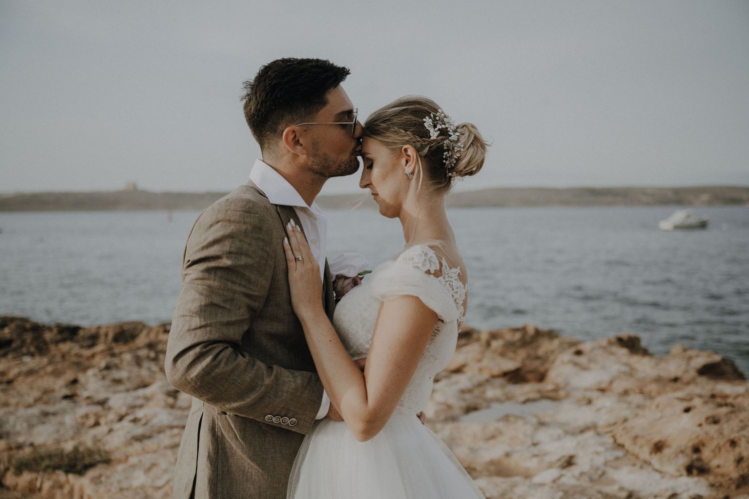 Tender moment between newlyweds on rocky beach during wedding photoshoot.