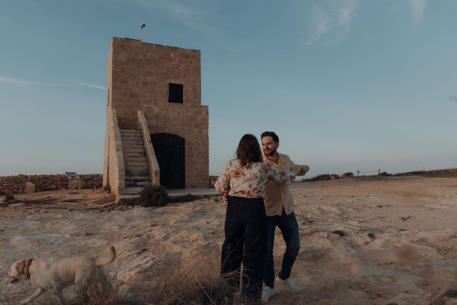 Two people walk together near an old stone structure in a desert setting.