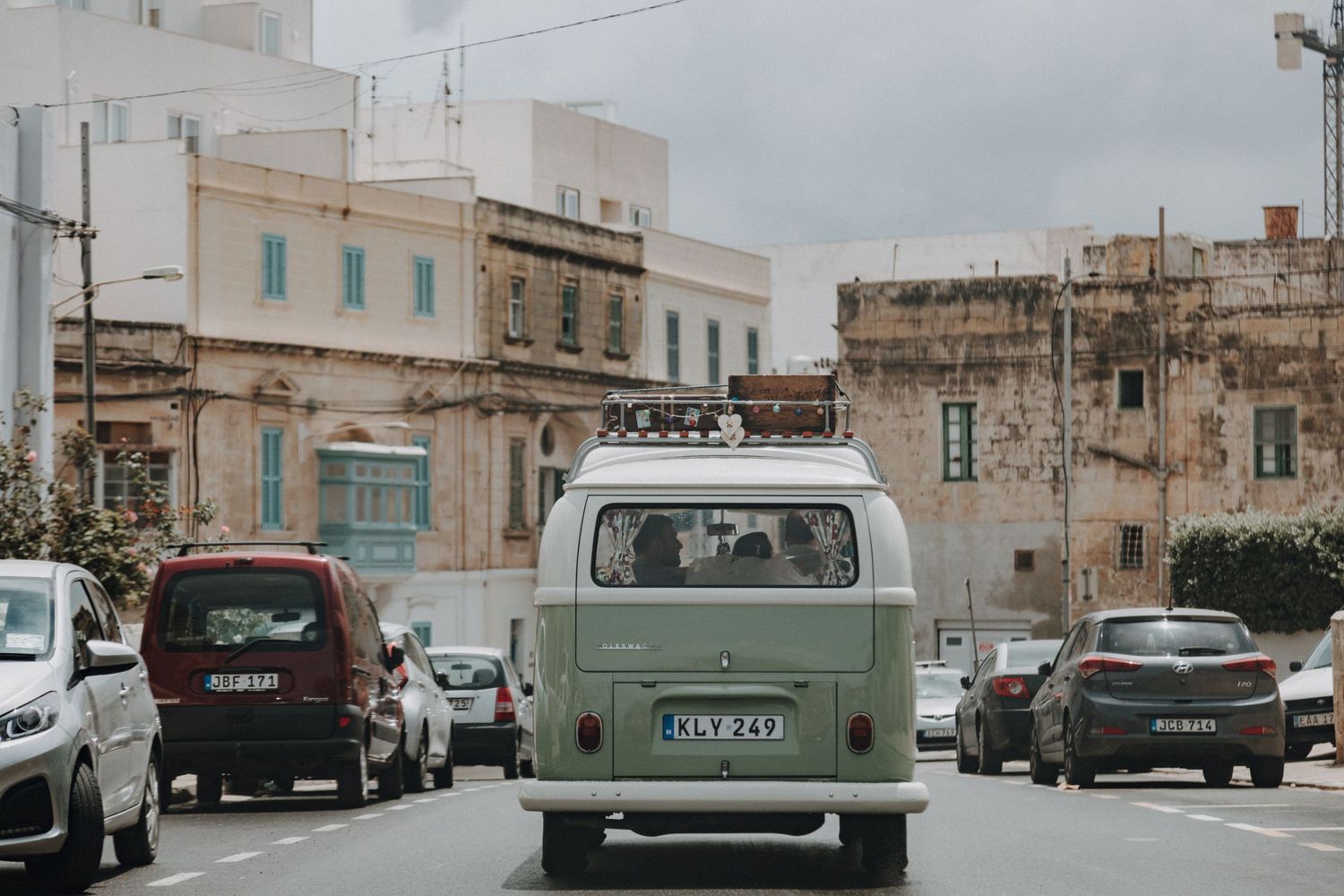 A vintage mint green VW van drives through an old Mediterranean street.