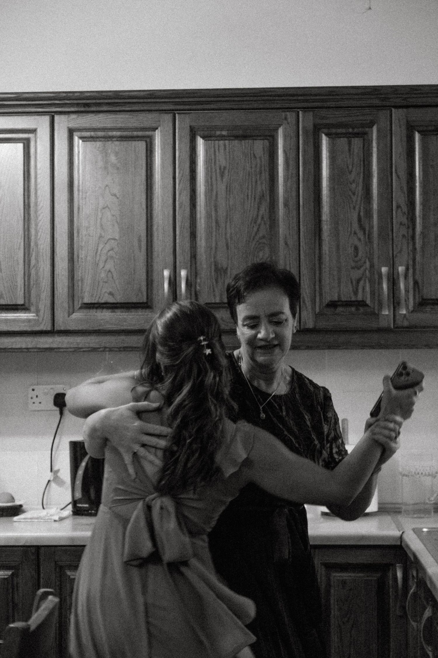 Intimate black and white moment of two people embracing in a kitchen.