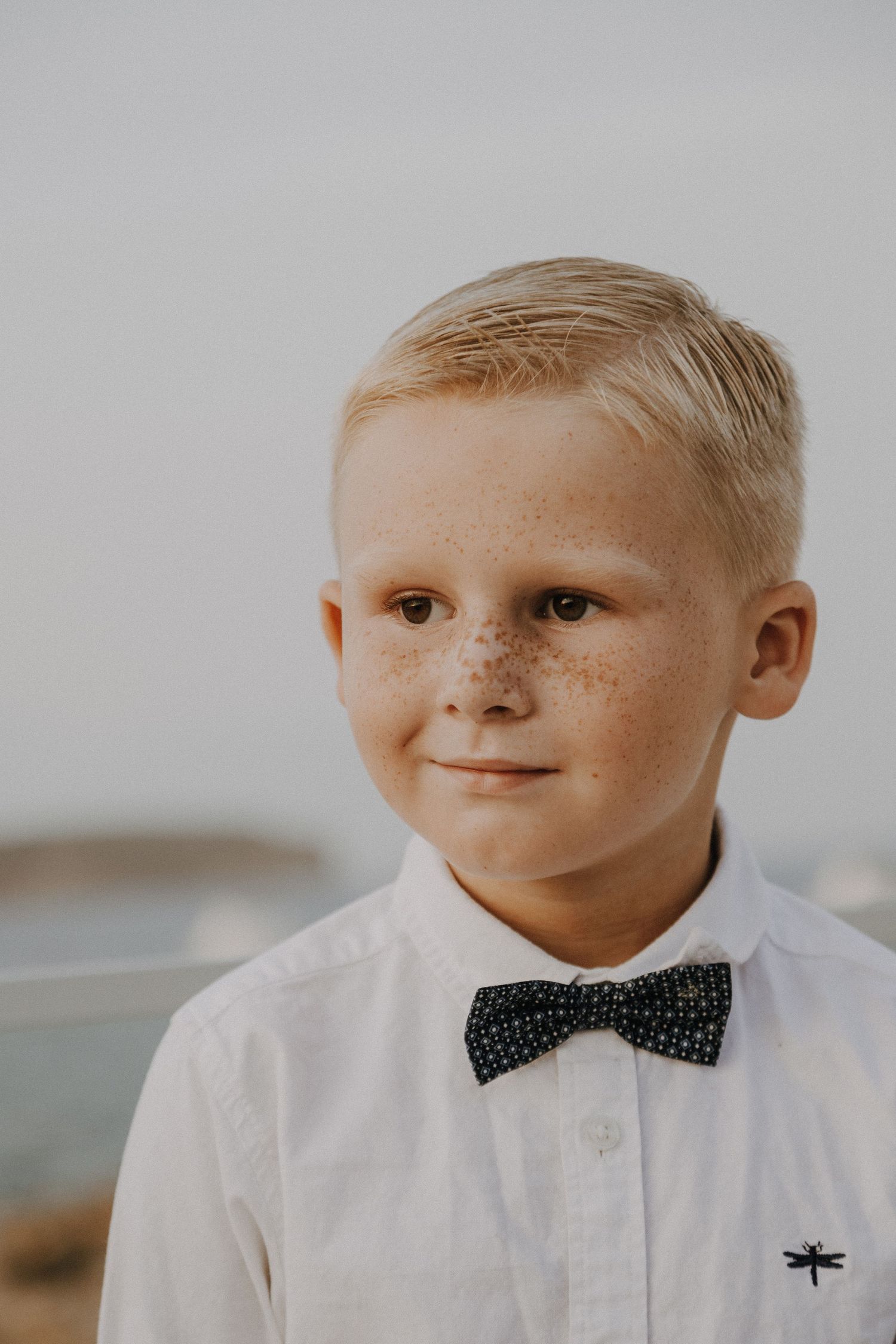 Portrait of young boy in crisp white shirt and polka dot bowtie against neutral background.
