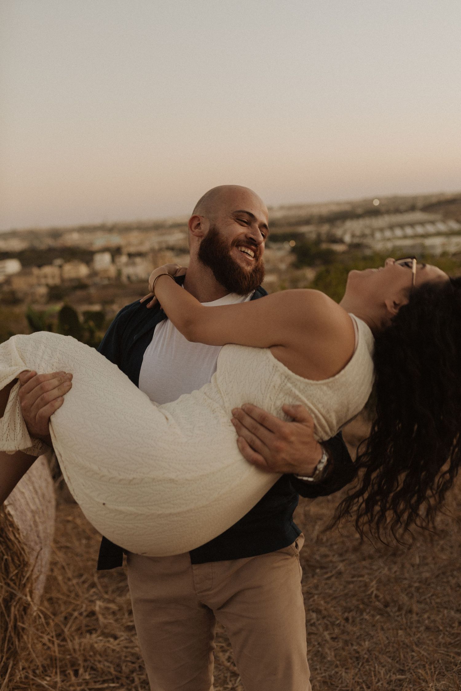 A romantic sunset portrait with a Mediterranean town visible in the background.
