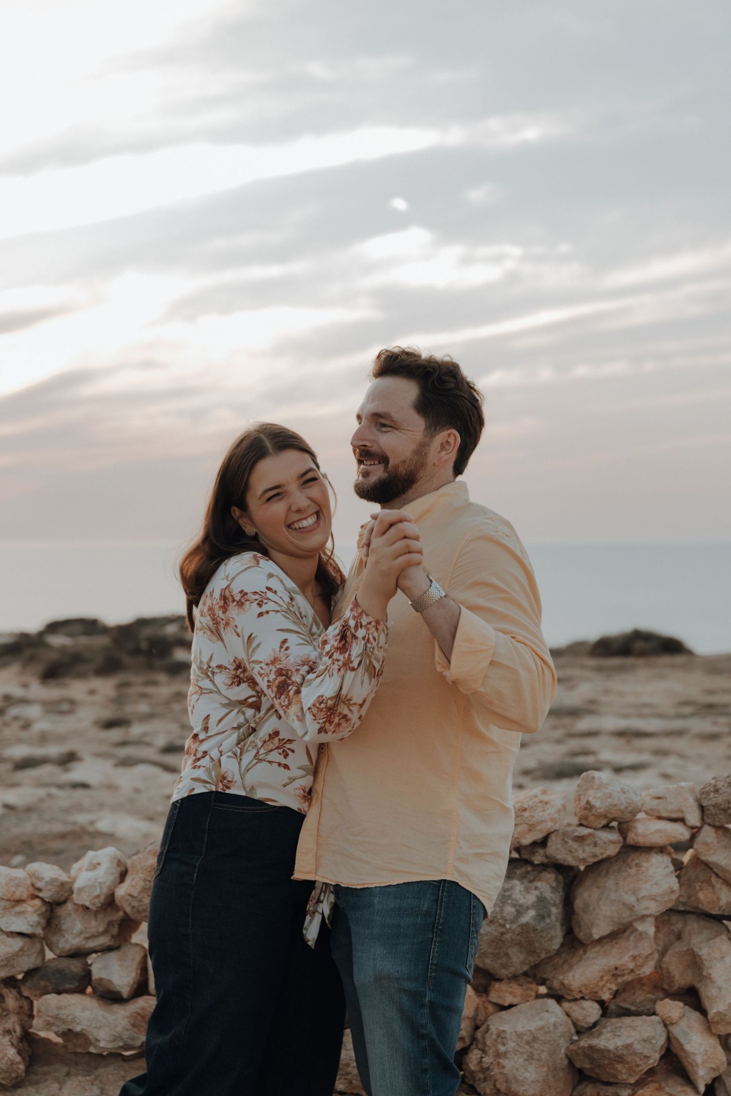 A couple shares a joyful moment together while standing on rocky terrain during sunset.