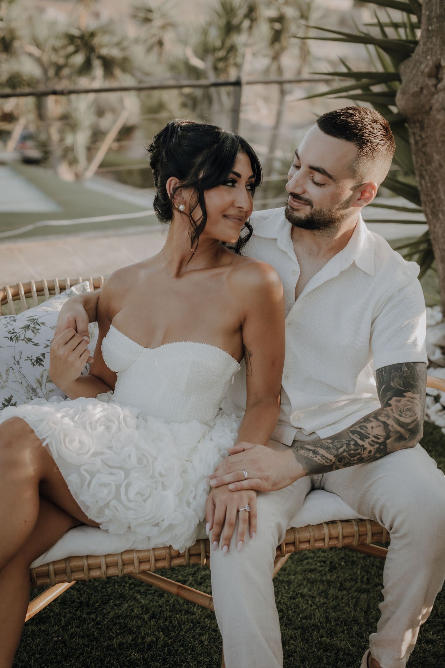 A couple shares an intimate moment while seated in rattan furniture during their wedding shoot.