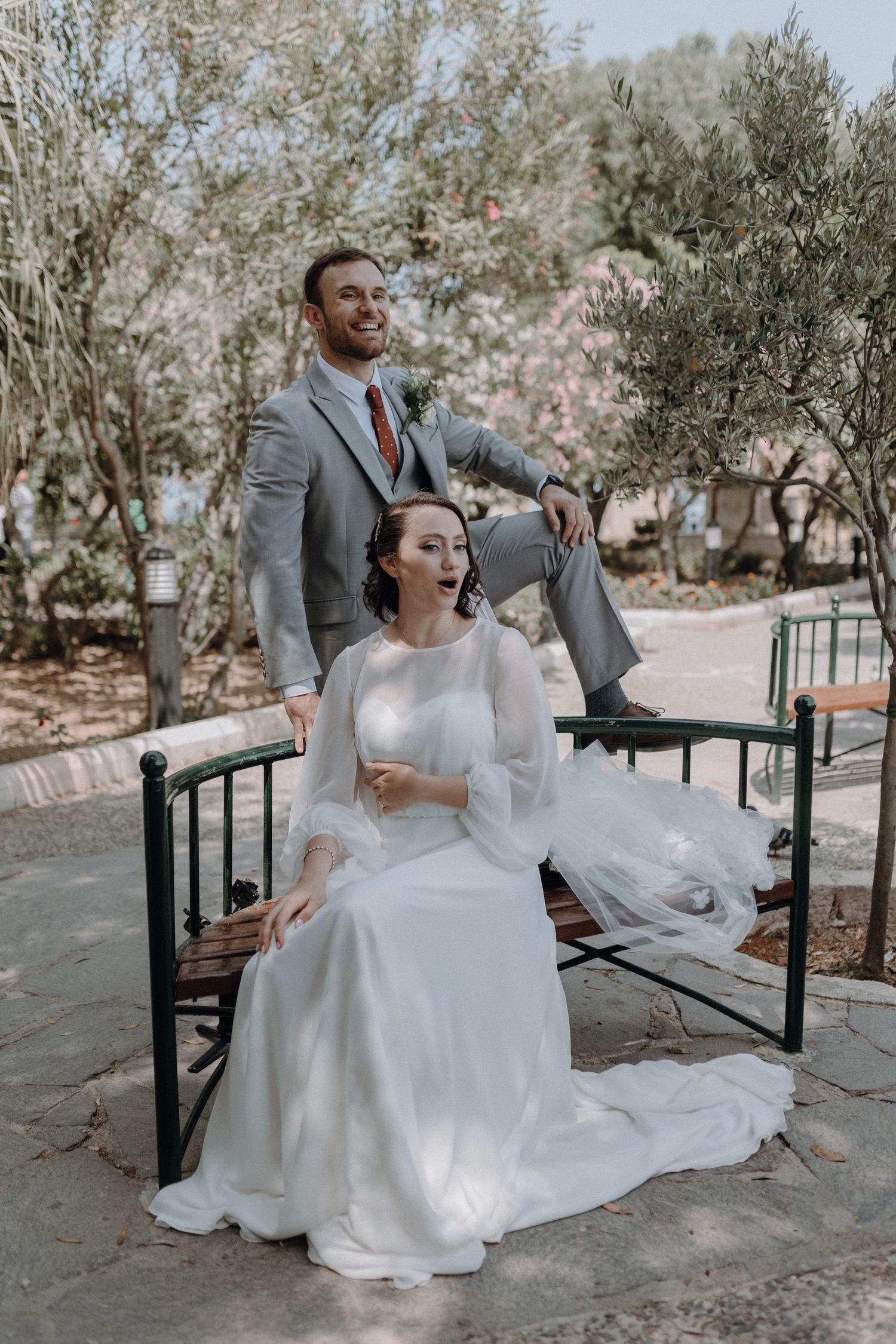 Artistic wedding portrait on garden bench with olive trees.