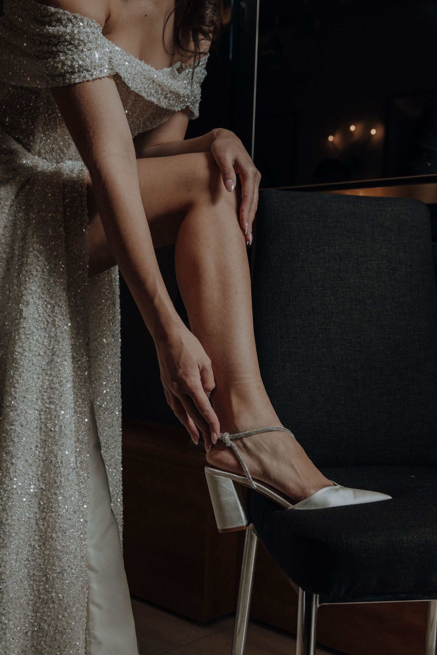 Close-up of bride in sparkly dress adjusting her shoe while sitting.