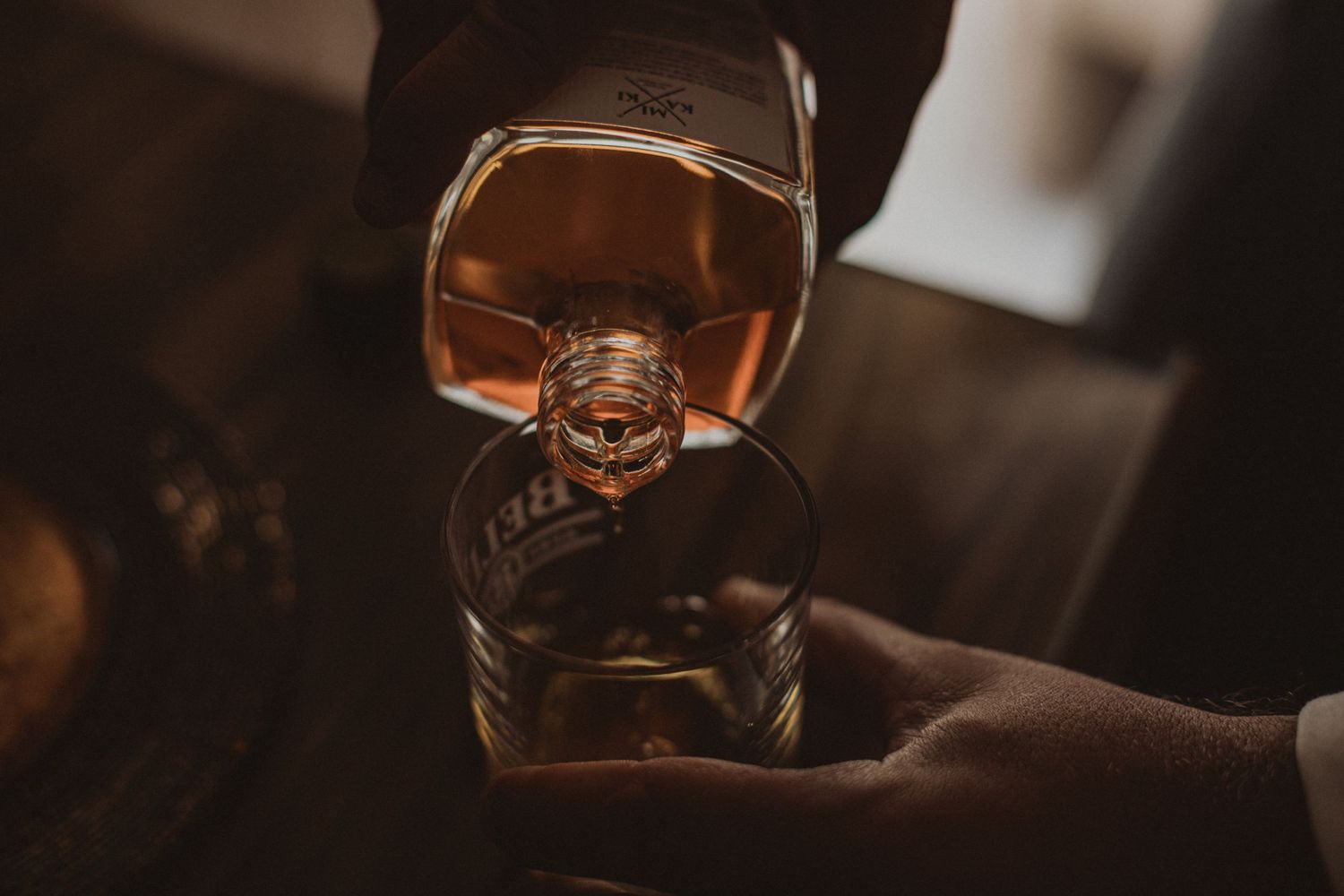 A glass of amber-colored spirits being held against a dark background.