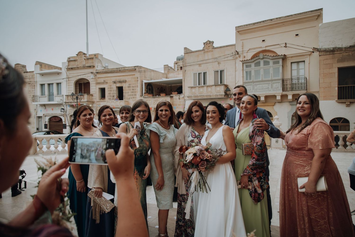 Wedding party poses together for group photo in front of ornate Mediterranean architecture.