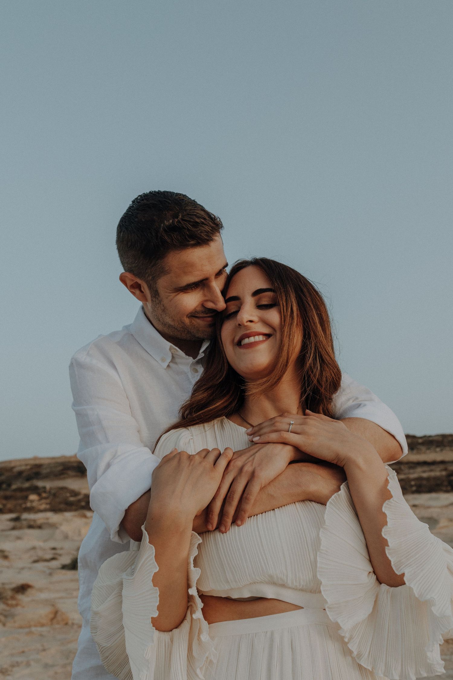 A romantic couple shares tender moments on a rocky beach at sunset.