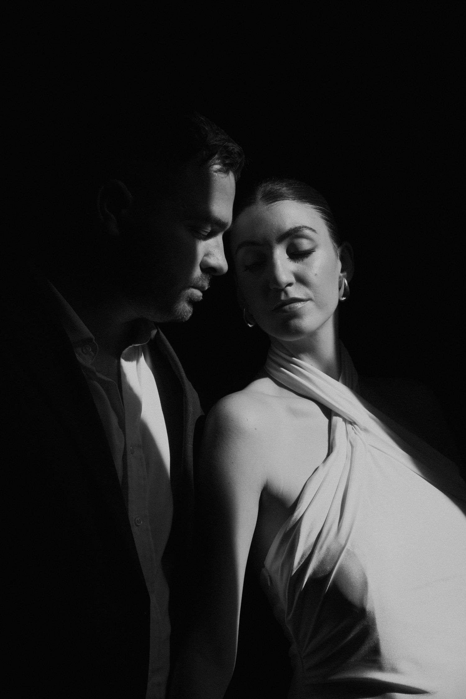 Dramatic black and white portrait of couple in intimate pose with contrasting shadows.
