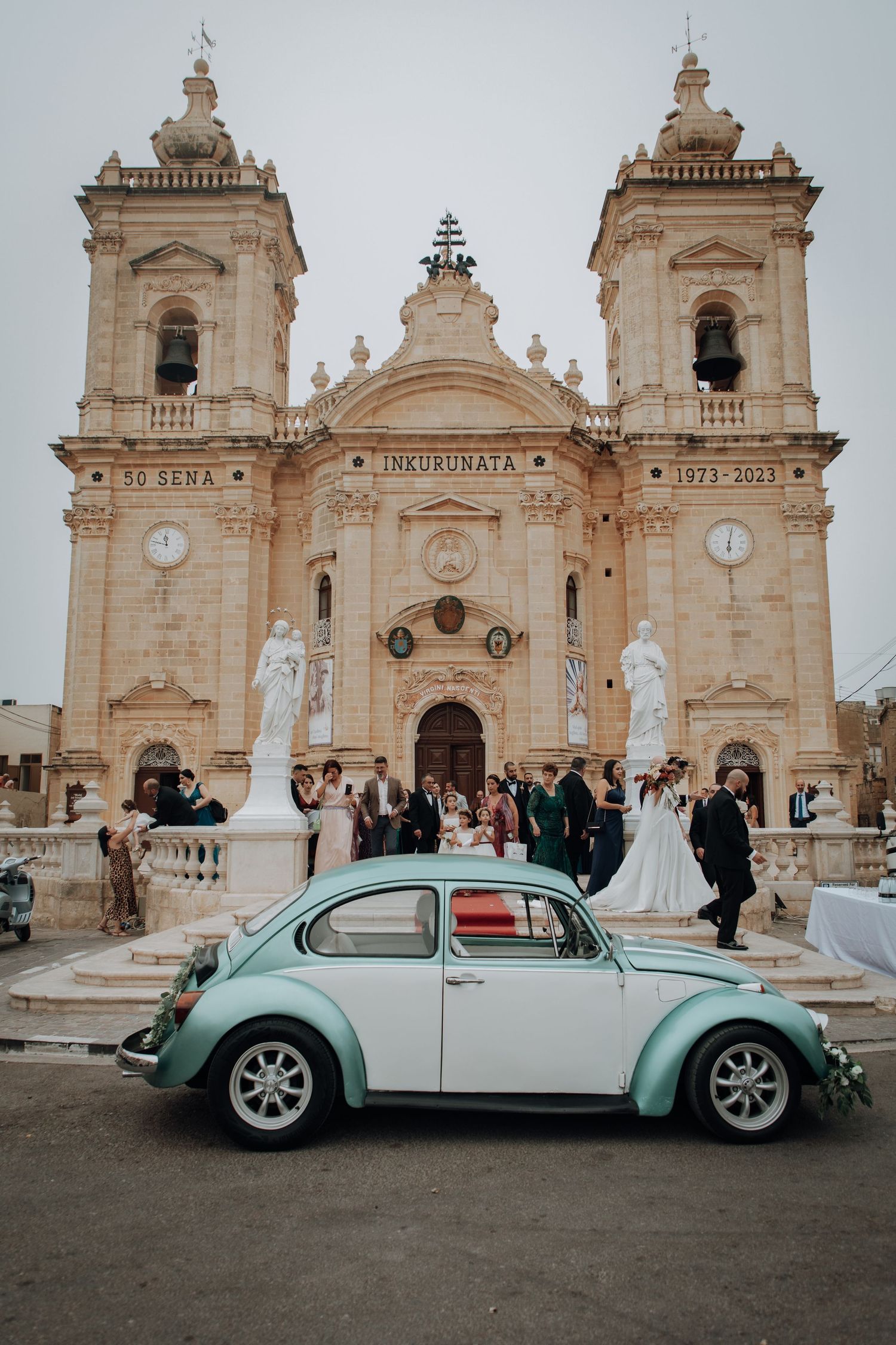 Classic VW Beetle parked in front of a grand Baroque church during a Mediterranean wedding celebration.