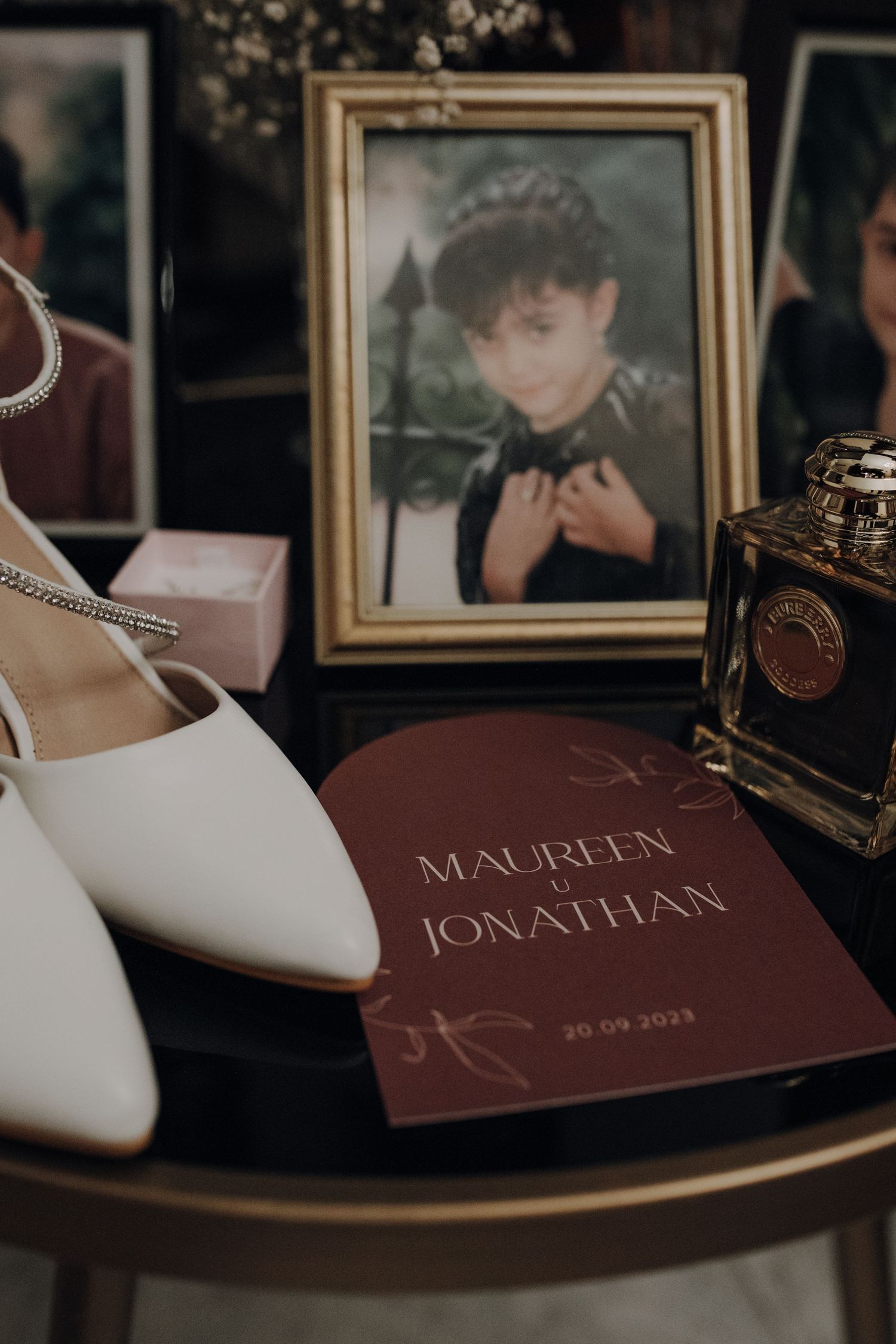Wedding detail flat lay with white shoes, invitation card, and vintage photograph in ornate frame.