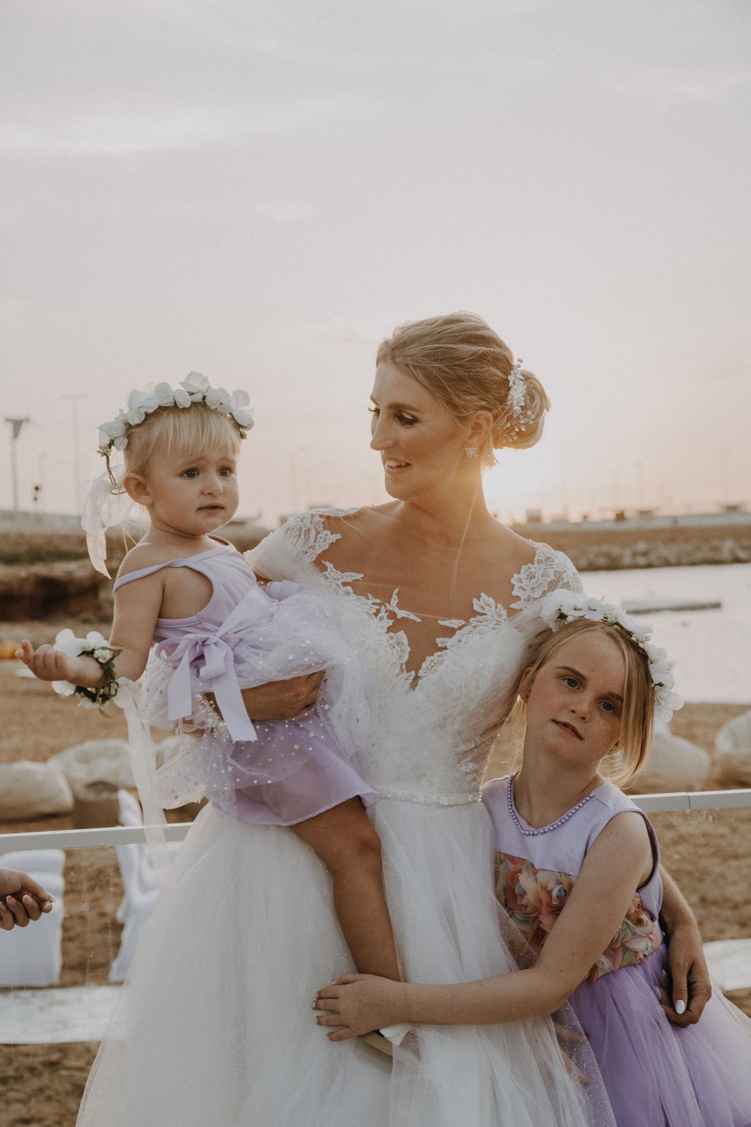 Candid wedding moment captured with bride and young attendants against sunset backdrop.