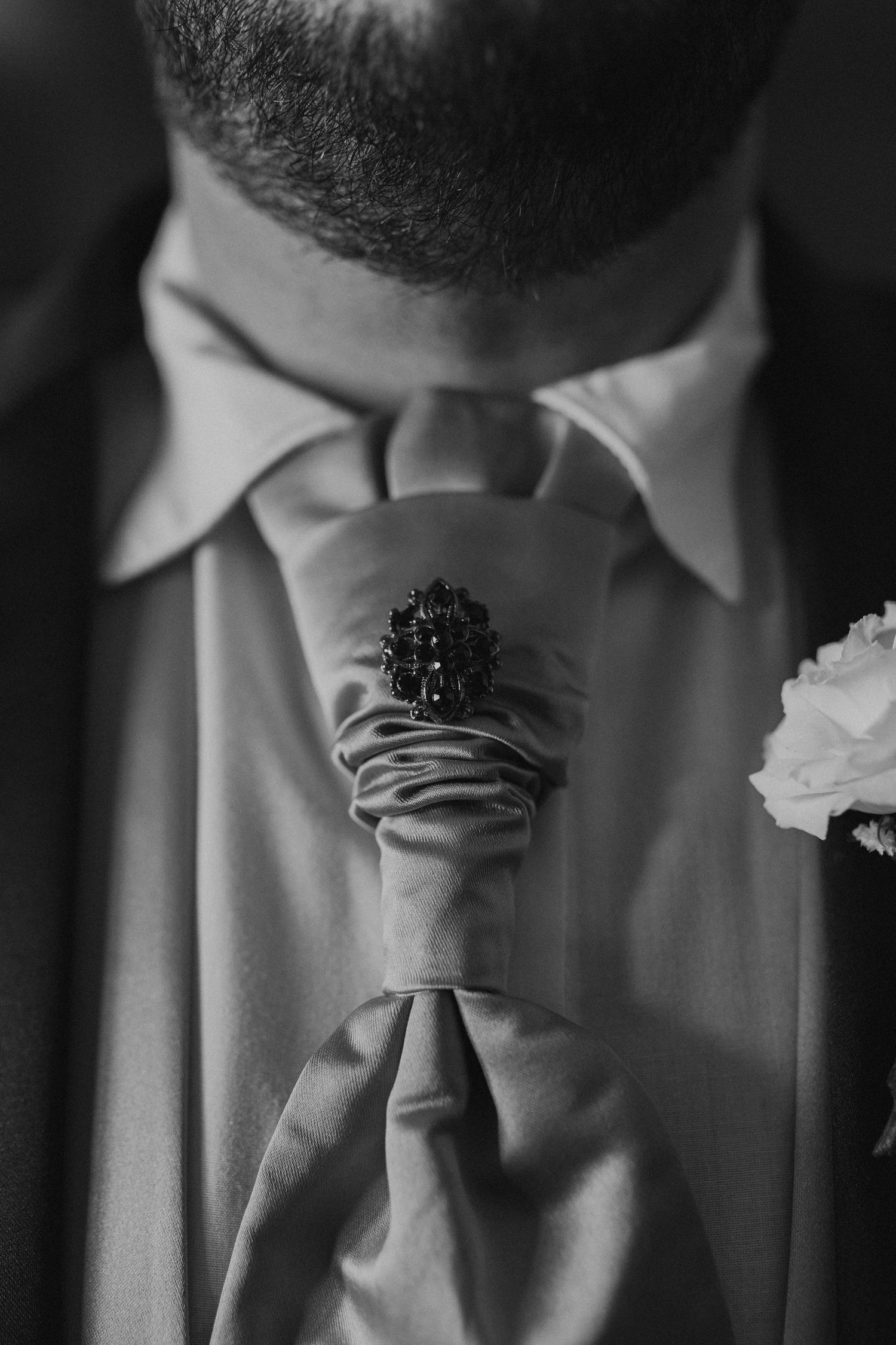 Close-up detail of a formal necktie knot and collar in black and white.