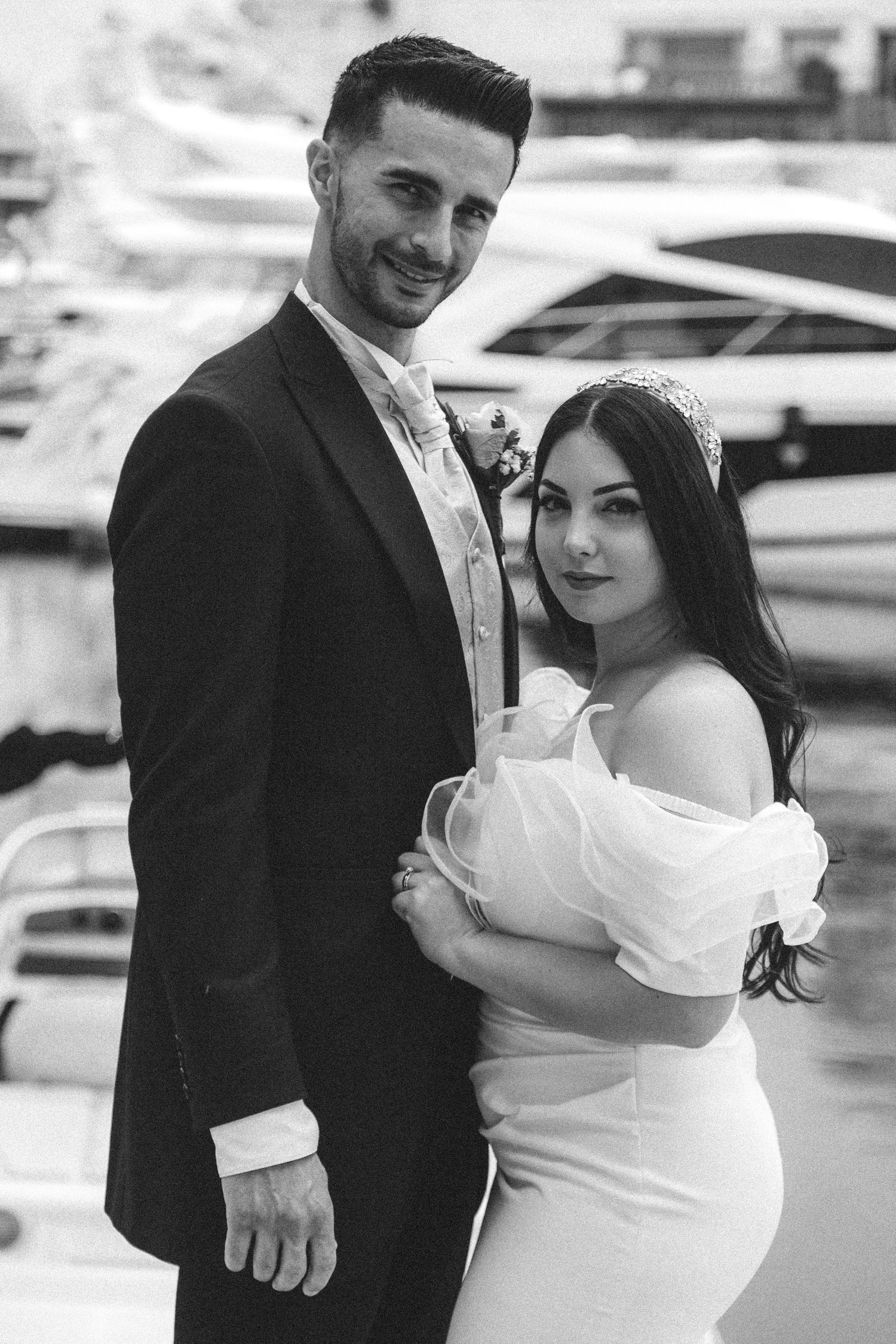 Bride and groom share intimate moments by boats in a marina during their wedding photoshoot.