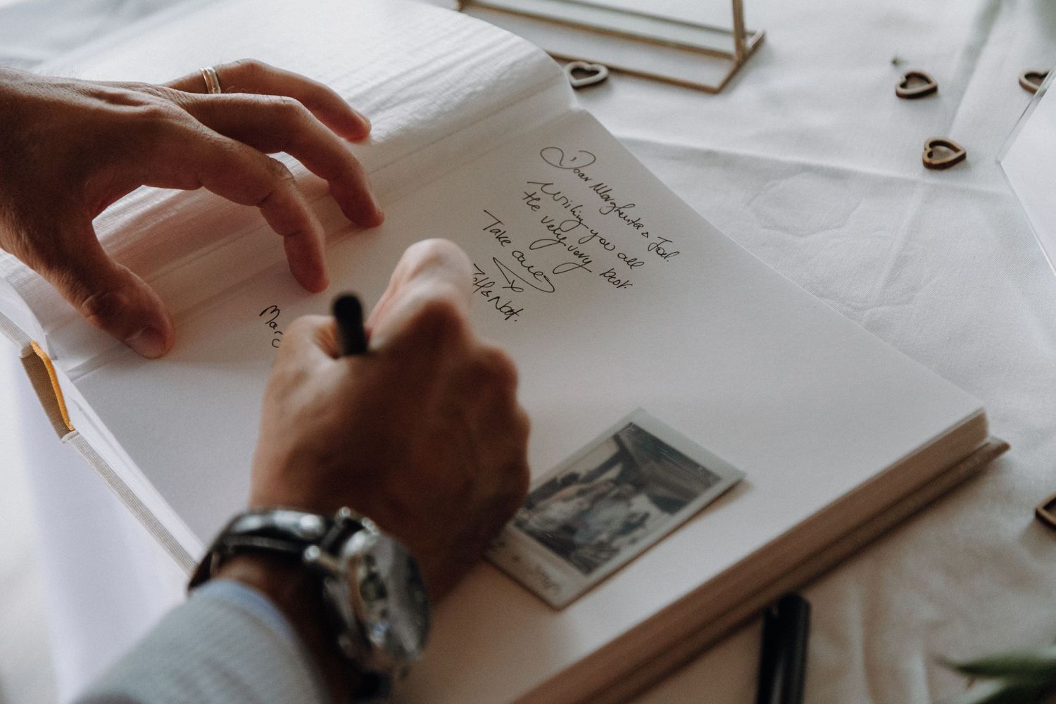 Someone writing in a guestbook or journal with a vintage photo on white paper.
