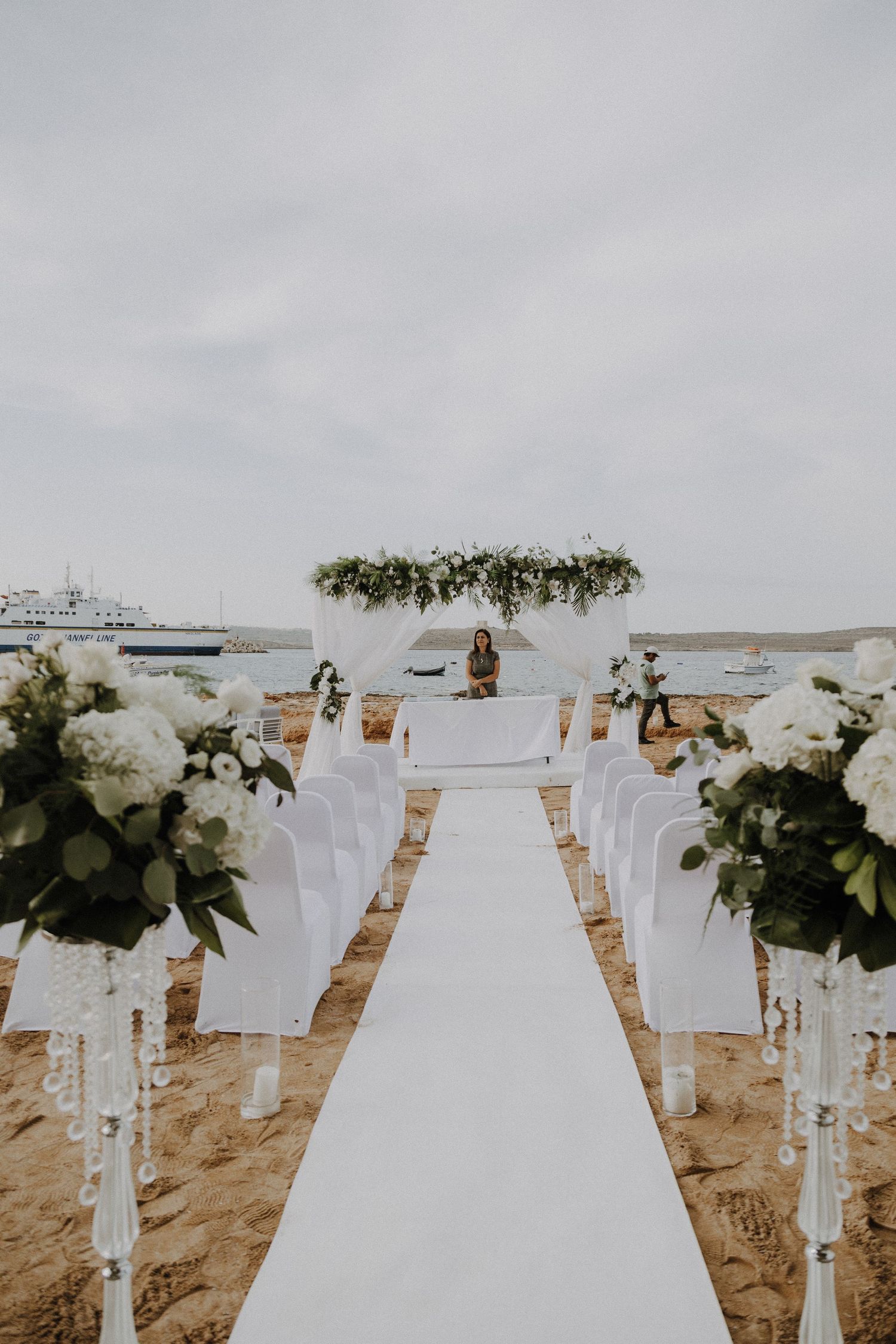 A beachfront wedding ceremony setup with white chairs, floral arrangements, and an ocean view backdrop.