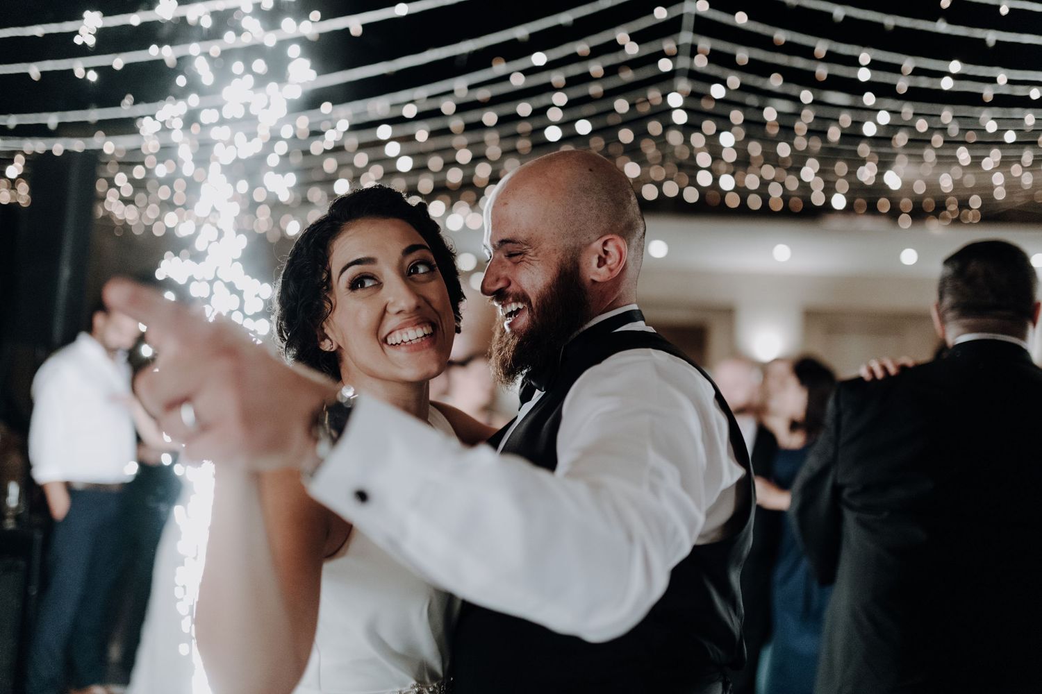 Newlyweds dancing together under romantic string lights at their wedding reception.