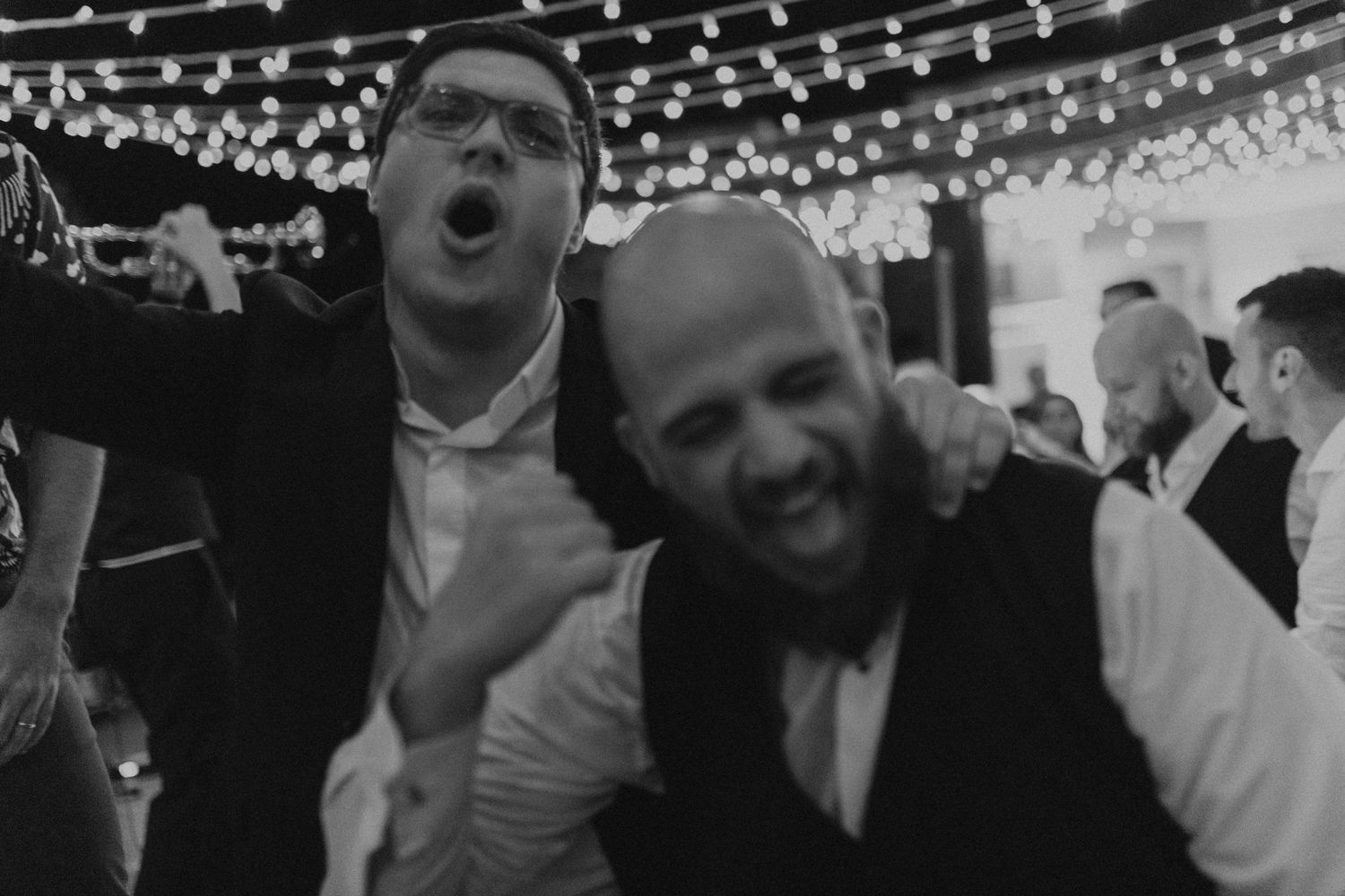 Black and white photo captures energetic dancing and celebration at wedding reception.