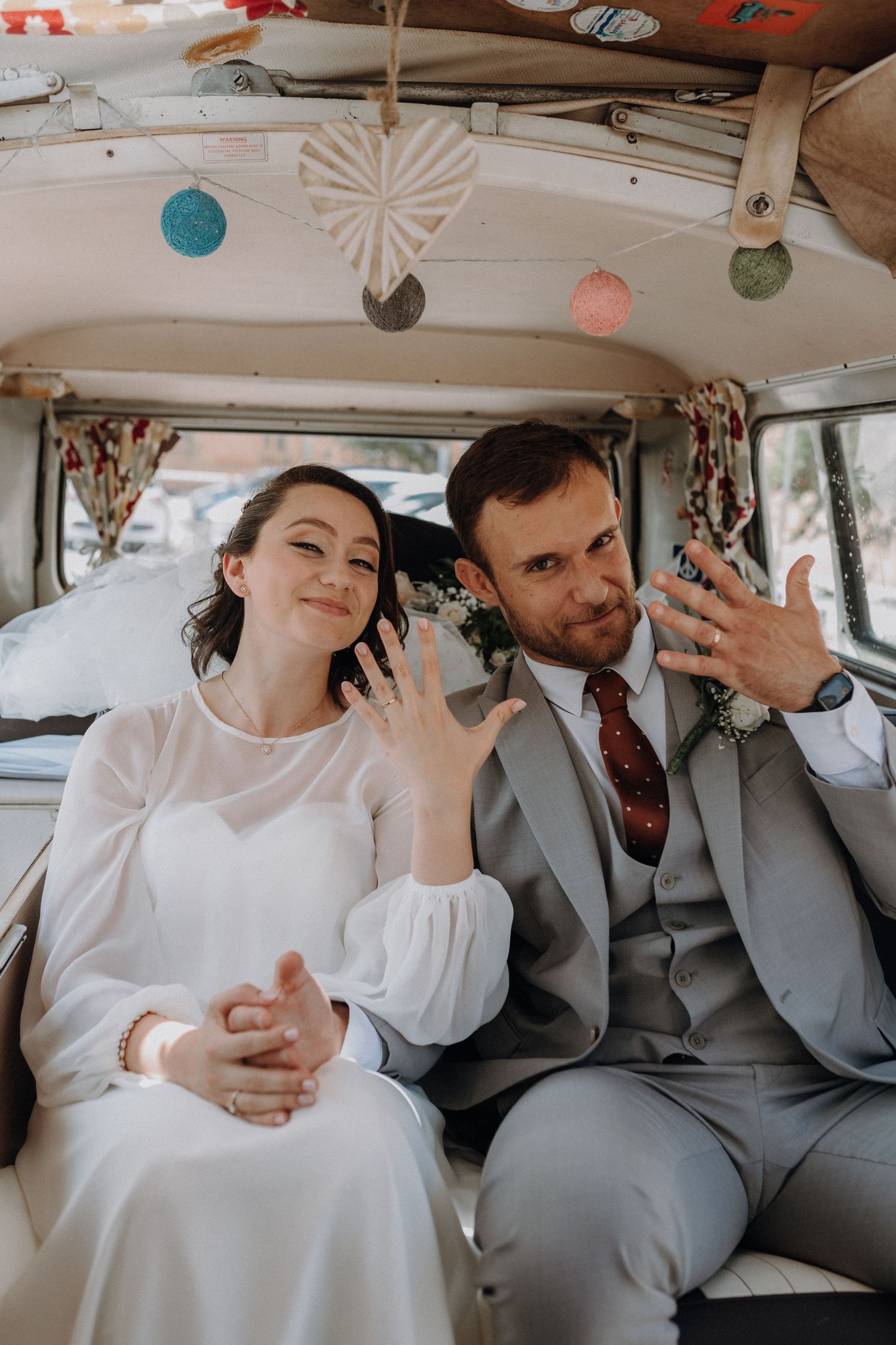 A couple shows off their rings while sitting in a vintage decorated van on their wedding day.
