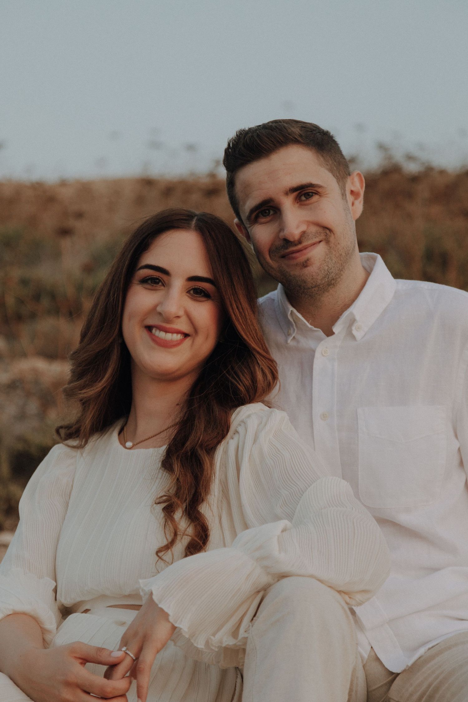 Couple in matching white outfits sharing romantic moment outdoors.