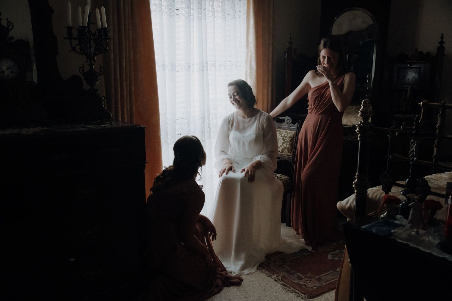 Wedding preparation scene in silhouette with bride and bridesmaids by window.