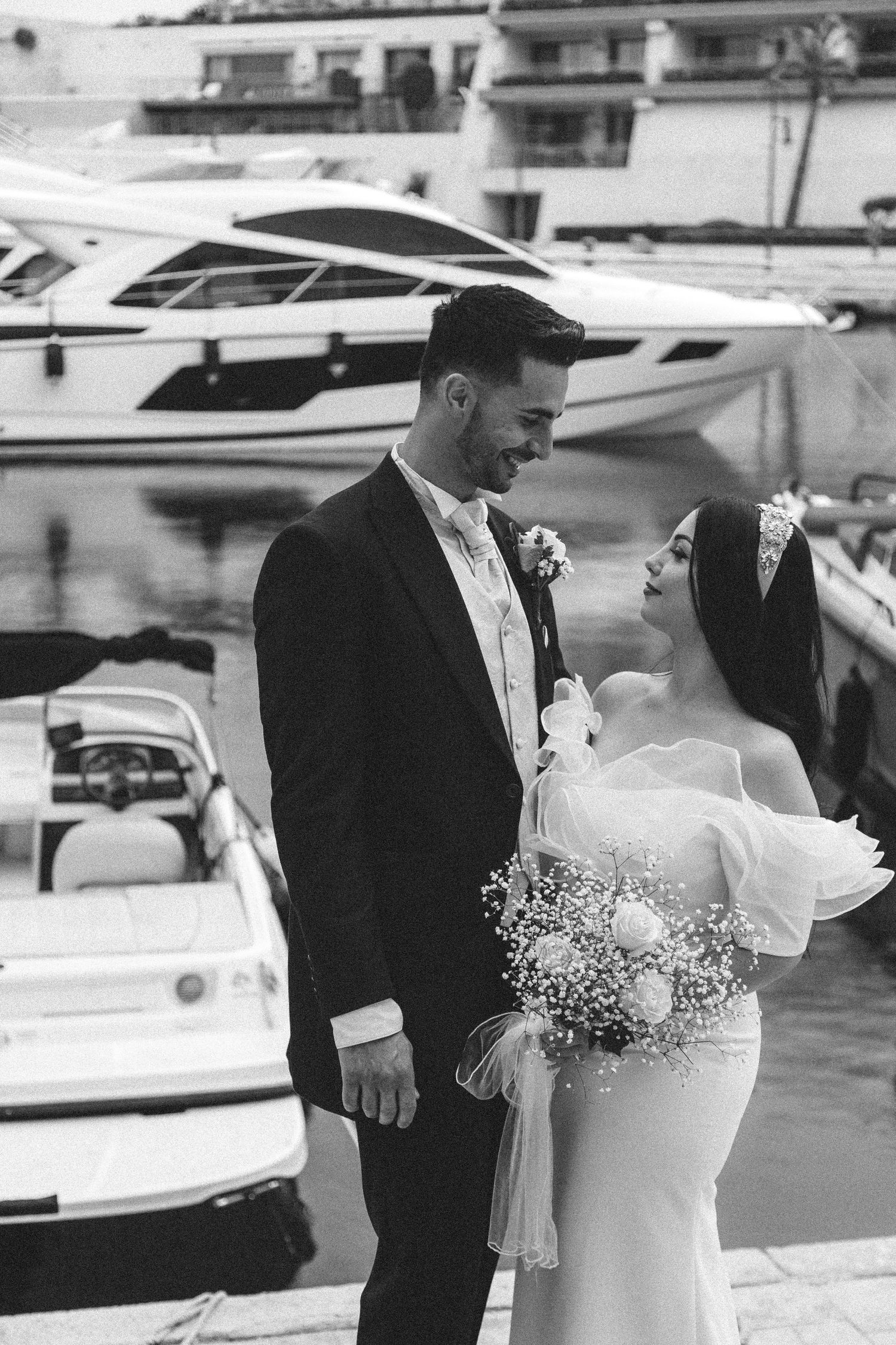Elegant couple poses together at a marina with luxury yachts in the background.
