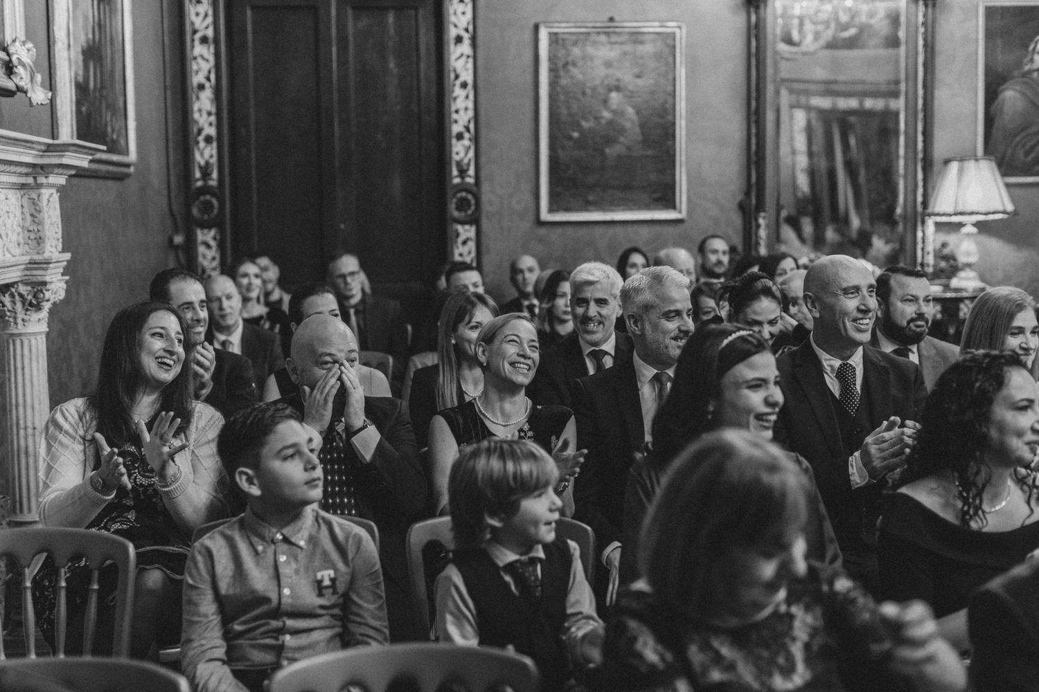 Wedding guests enjoying a lively reception in an ornate vintage room filled with laughter and celebration.