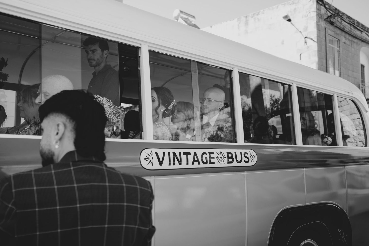 Black and white photo of vintage bus transporting wedding guests.