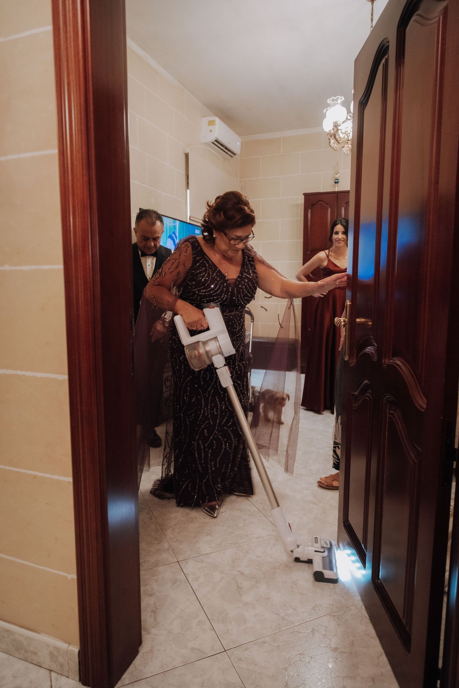 A person in a formal dark dress navigates through a doorway with cleaning supplies.