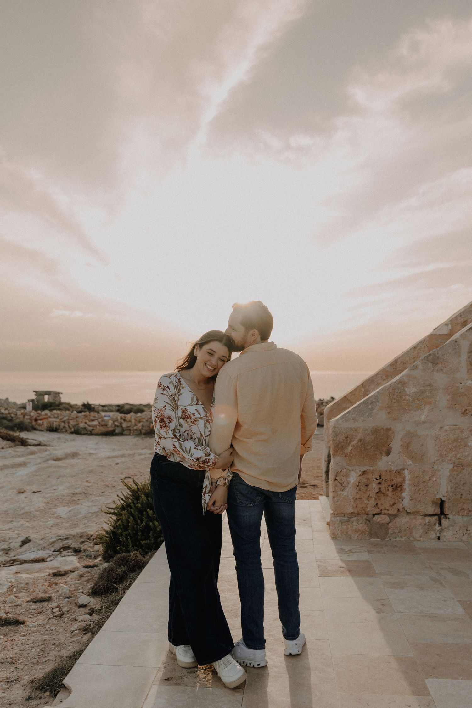 A couple embraces while walking along a path during sunset.