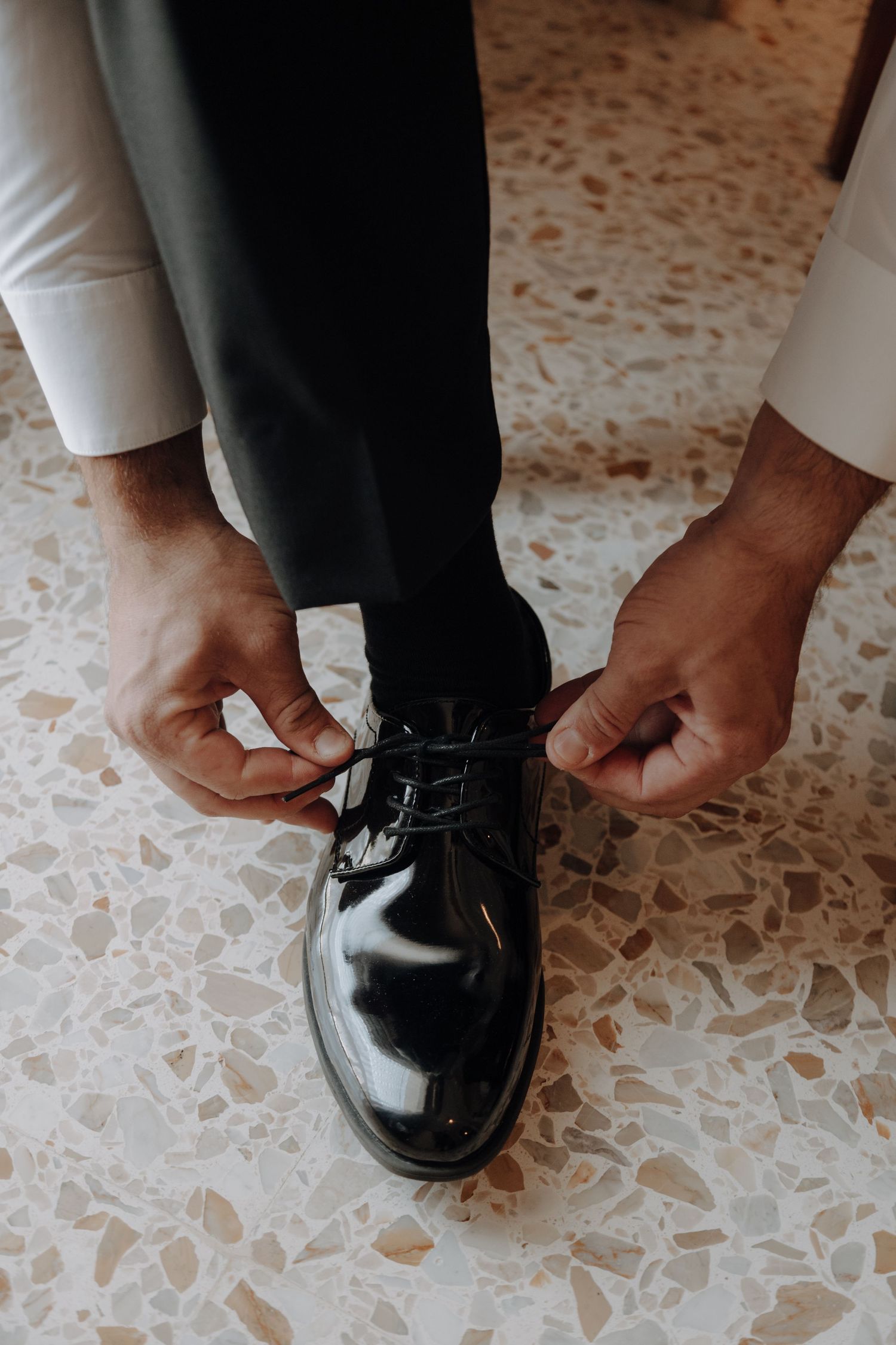 Close-up of hands adjusting formal black dress shoes on textured flooring.