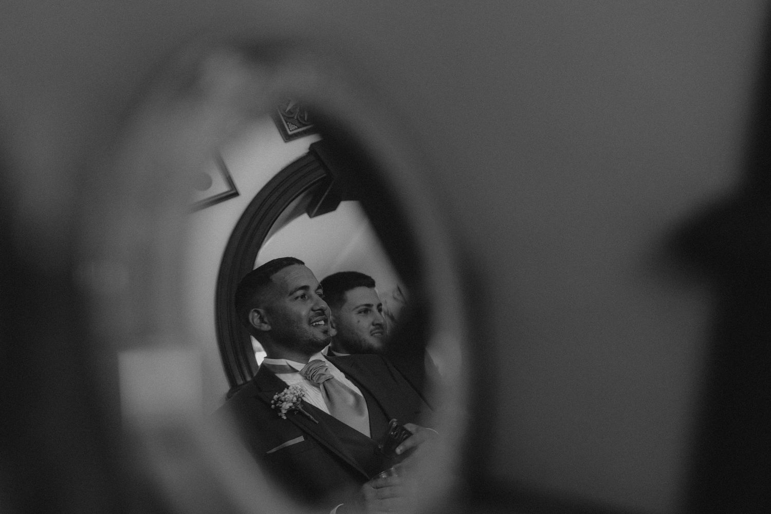 Black and white reflection of two men in formalwear viewed through a mirror.