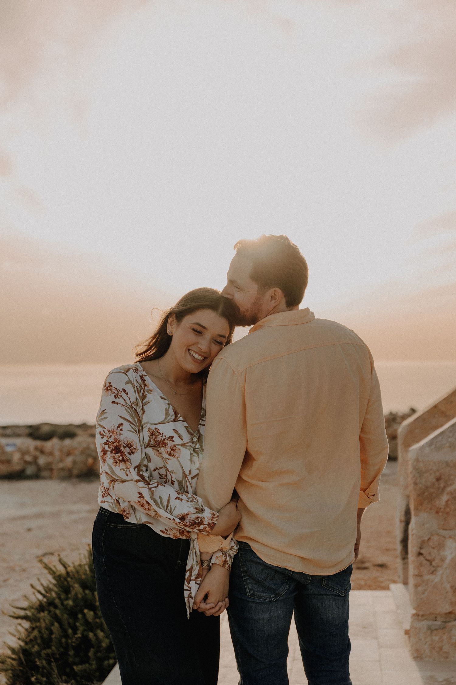 A couple shares a romantic moment at sunset against a desert landscape backdrop.