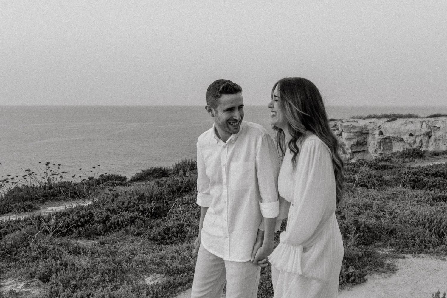 A romantic couple poses for photos on a scenic coastal overlook.