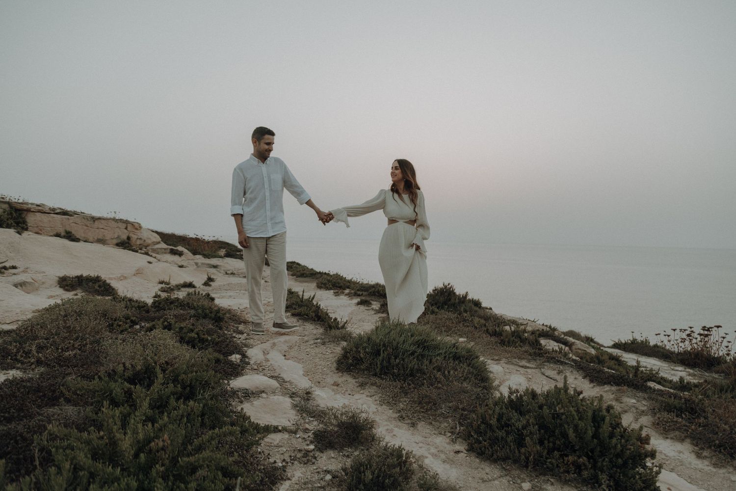 Couple walking together on coastal cliffs during an overcast day.