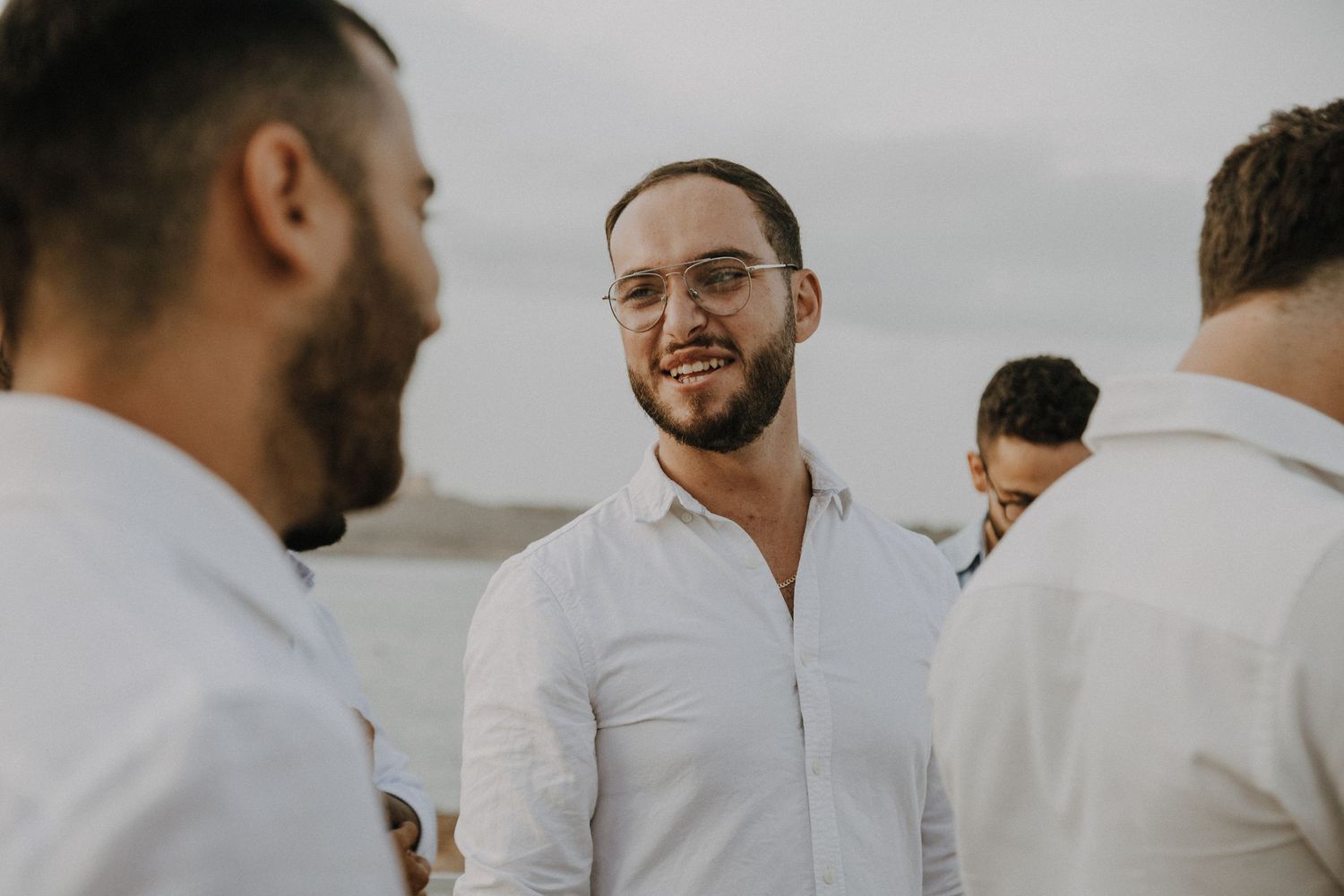 Candid moment of wedding guests in white shirts conversing at outdoor reception.