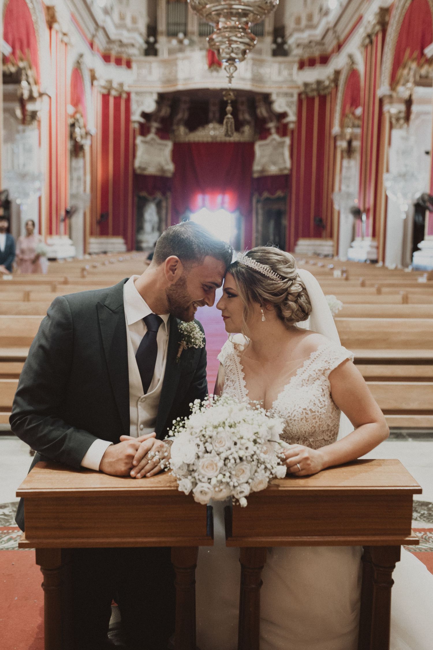 Wedding couple sharing intimate moment in ornate church with red and gold decor.