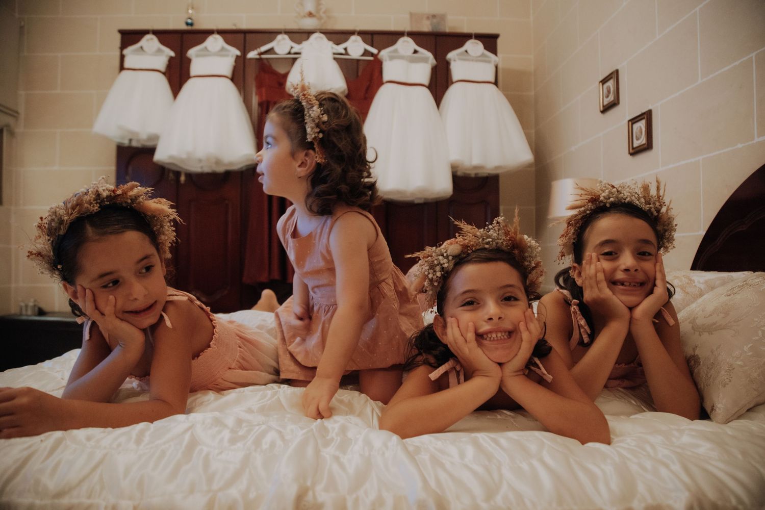 Young children in white dresses playfully posing on a white bed.