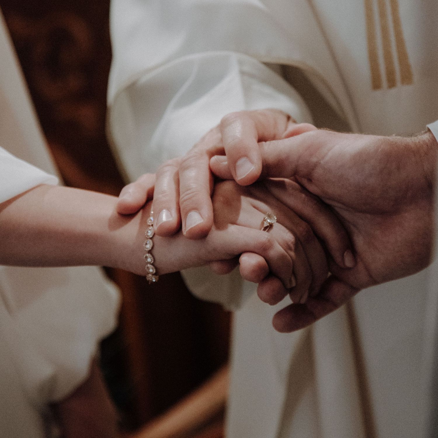 Intimate moment of hands clasped together showing wedding rings and bridal bracelet.