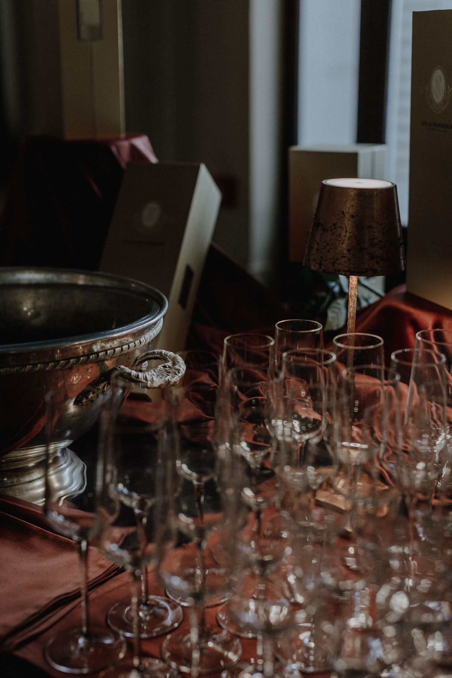 Collection of empty wine glasses arranged on dark surface with lamp in background.