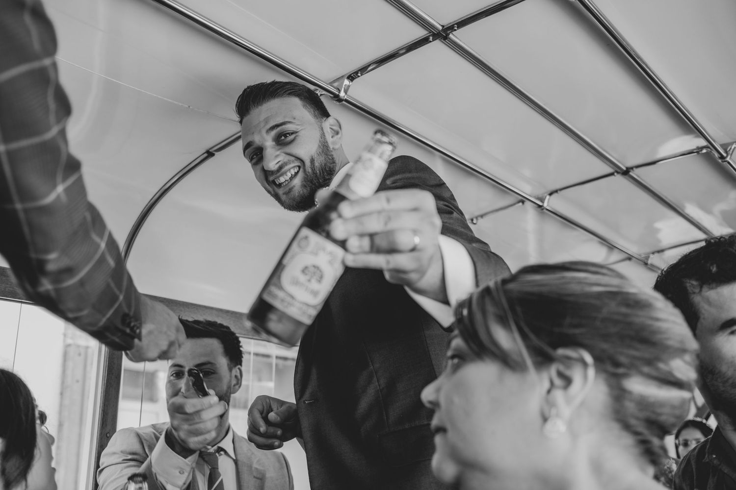Wedding guests celebrating with drinks inside vintage bus during celebration.