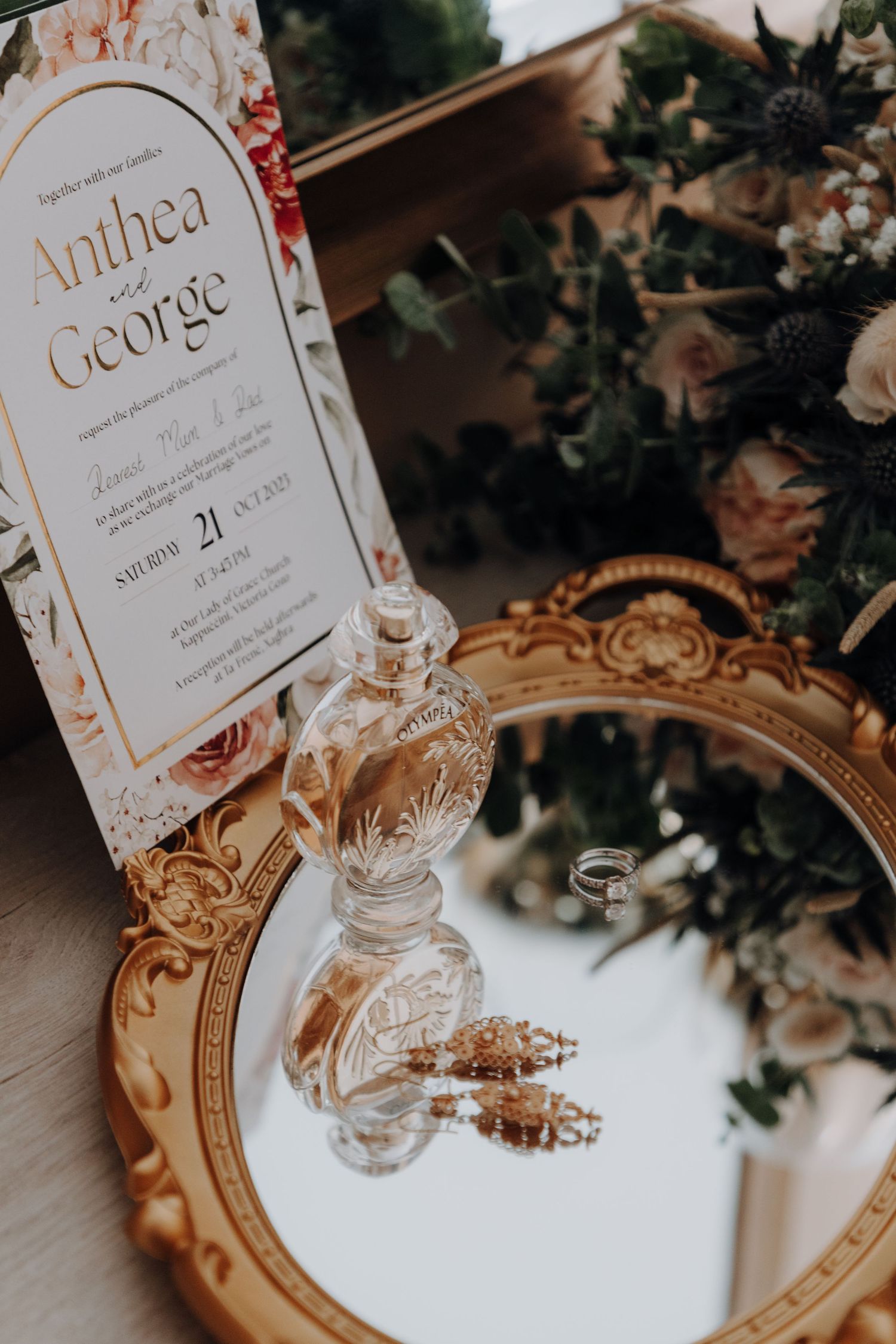 Elegant wedding invitations and perfume bottles displayed on an ornate gold mirror.