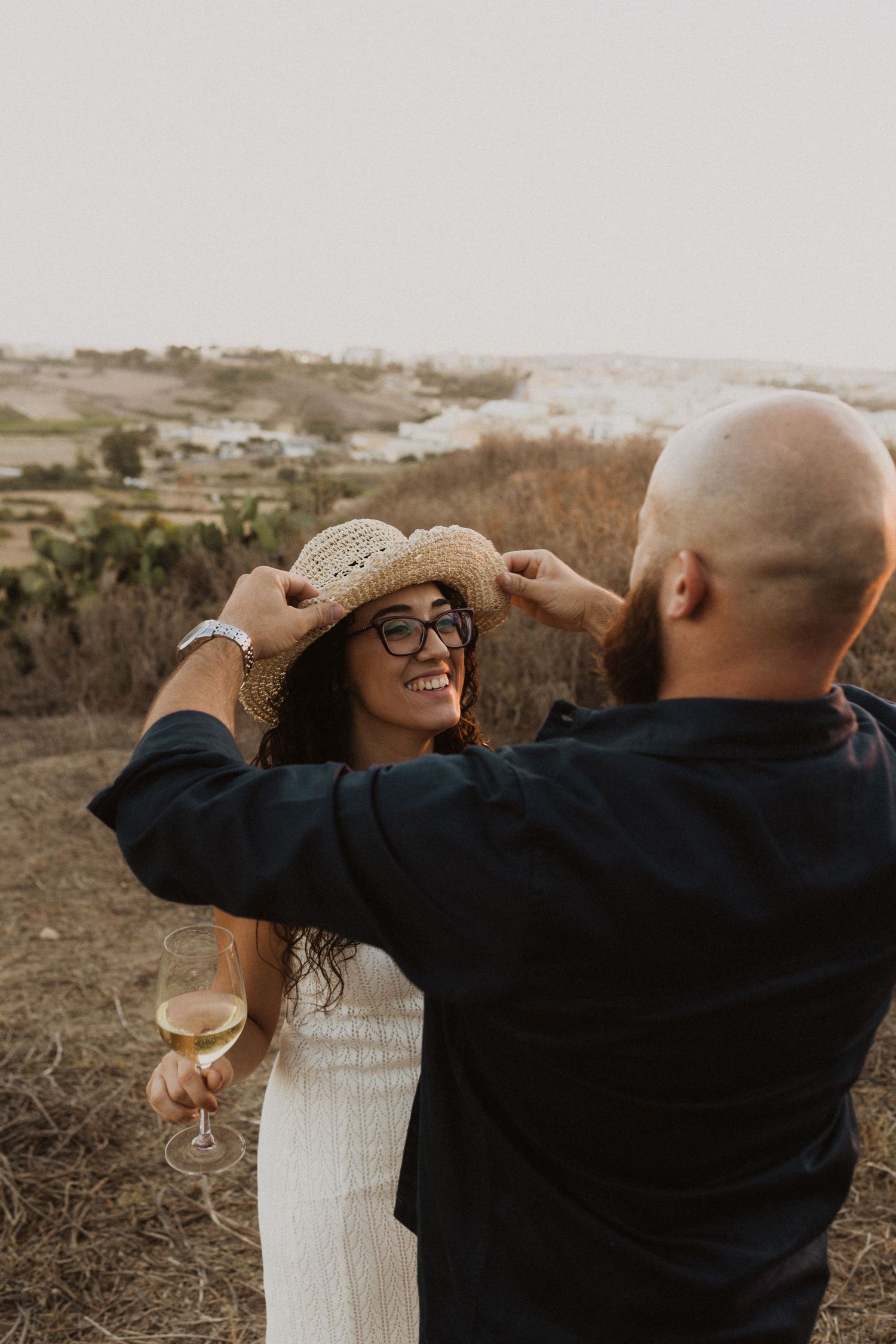 A couple playfully shielding their eyes from the sun during golden hour.