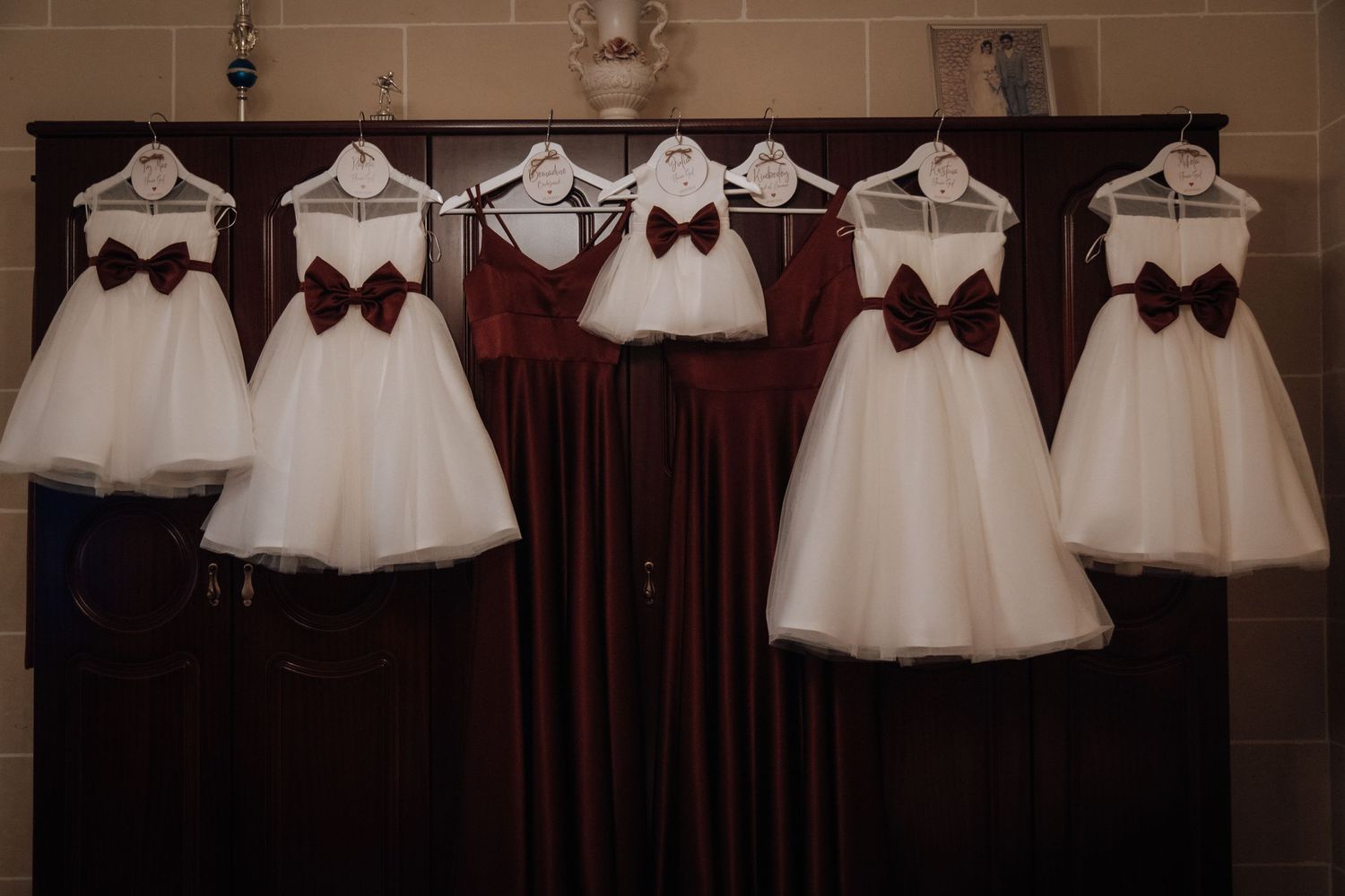 White formal dresses displayed on hangers against a dark curtain backdrop.