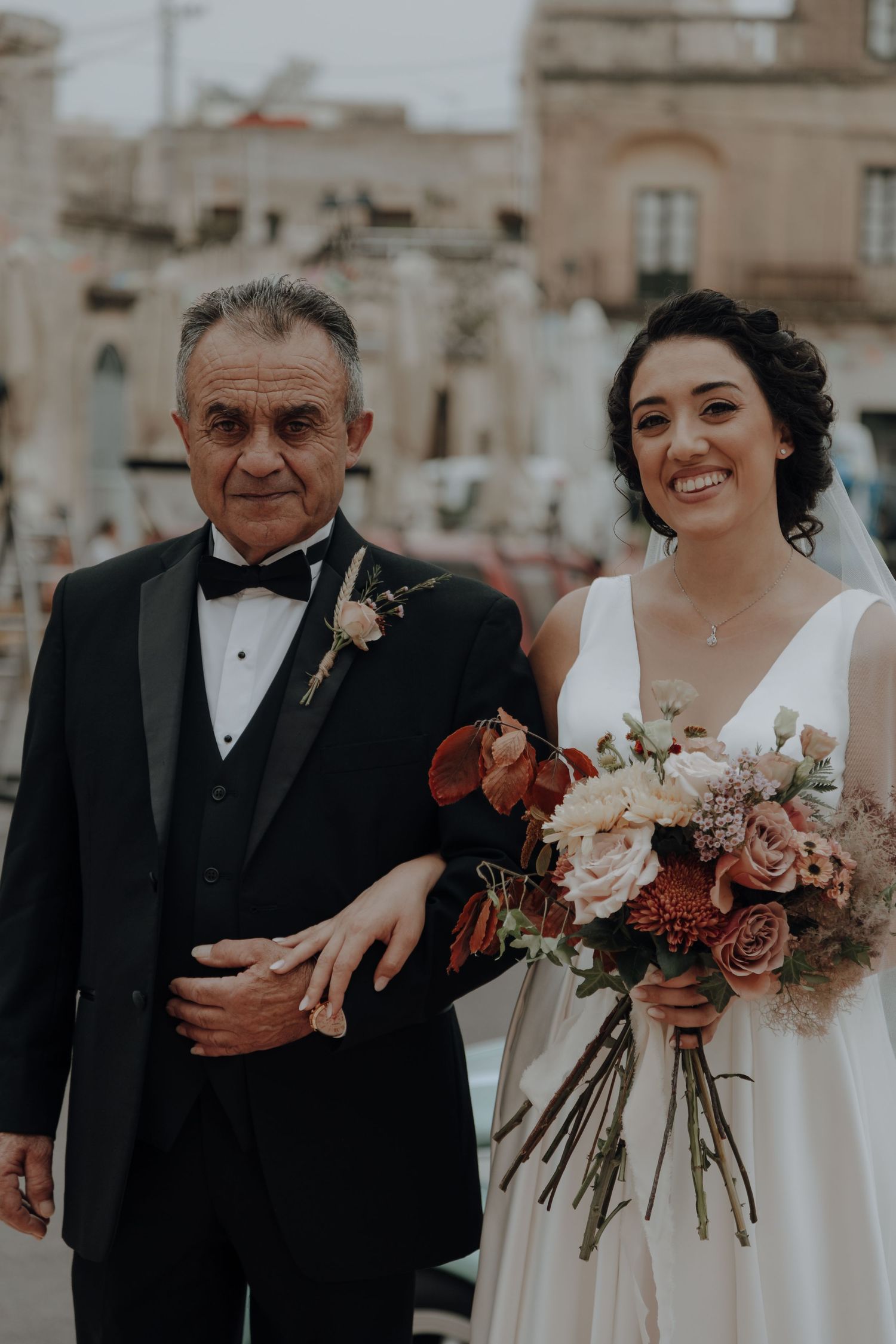 Bride in elegant white dress holds colorful bouquet while standing with companion.
