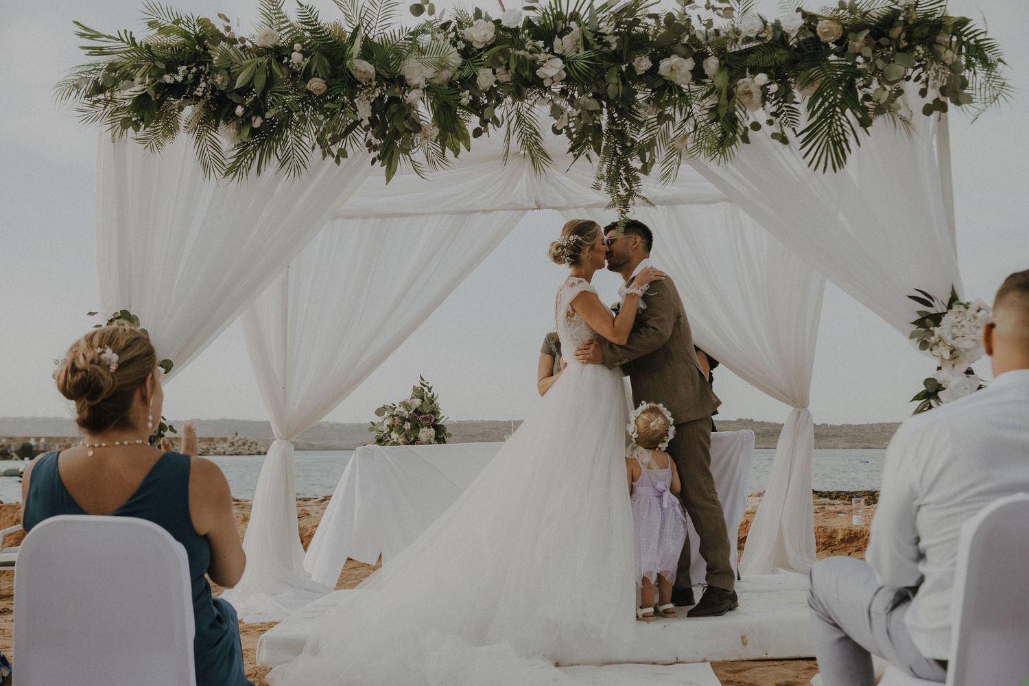 White draped canopy with tropical greenery decorations at oceanfront wedding venue.
